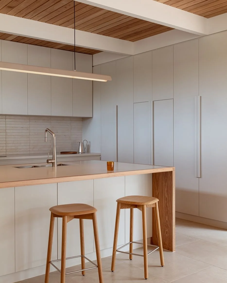 Modern kitchen with white cabinets, a wooden island with two stools, a sink, and minimalist decor.