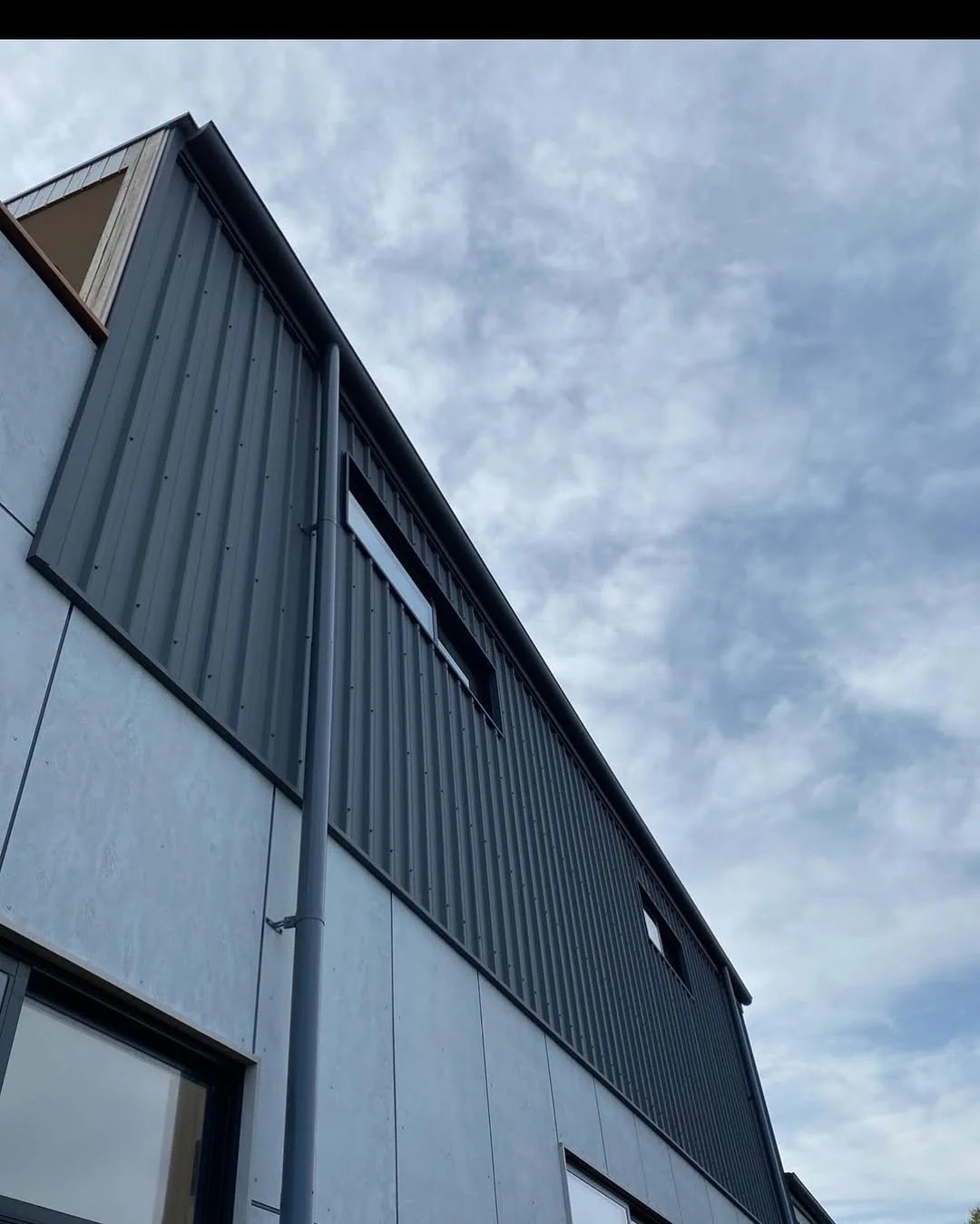 Close-up of a modern building with metal siding and windows, under a cloudy sky.
