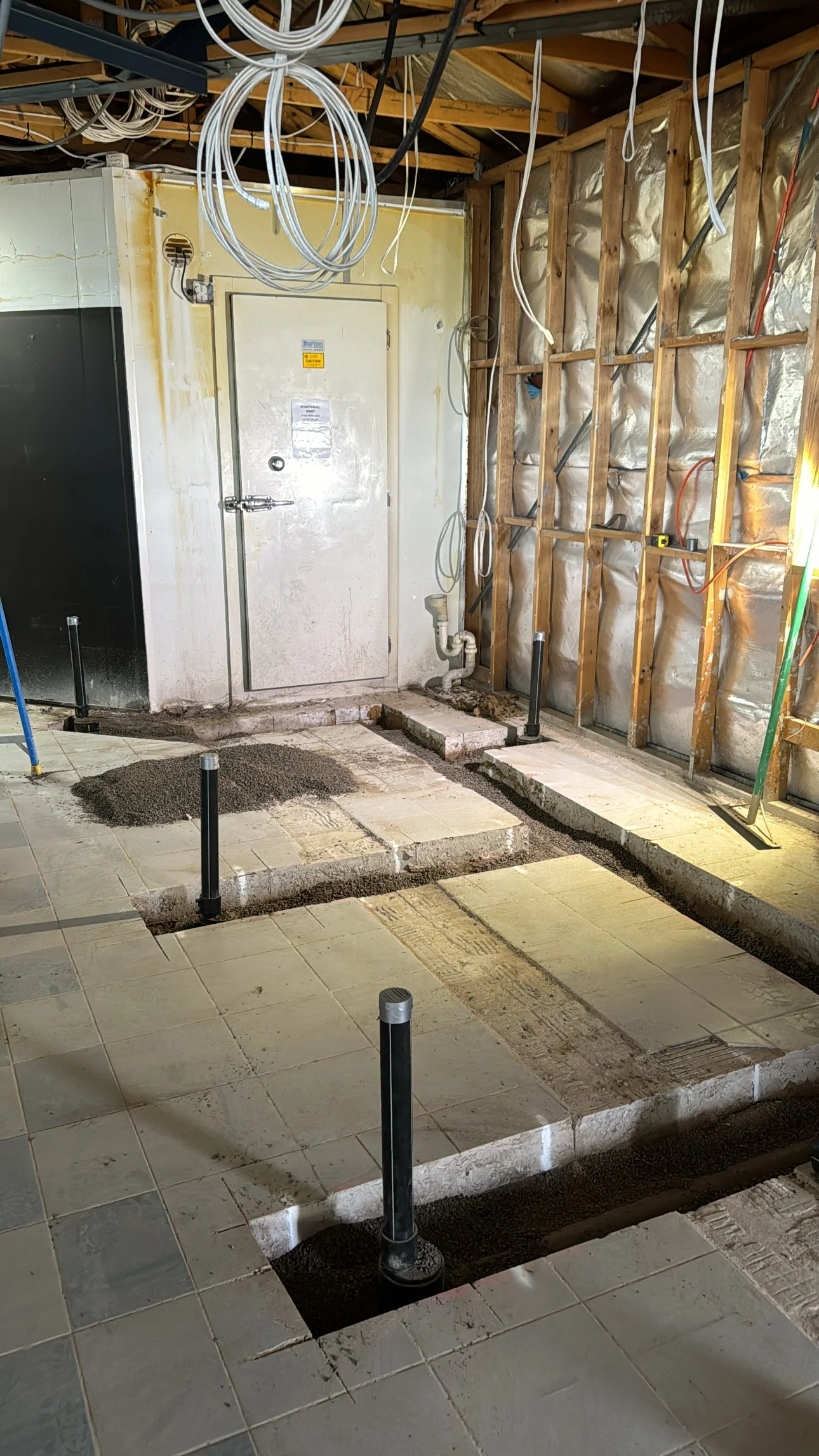 Under construction bathroom with exposed wall framing, plumbing pipes, and a raised floor area with concrete blocks and sand.