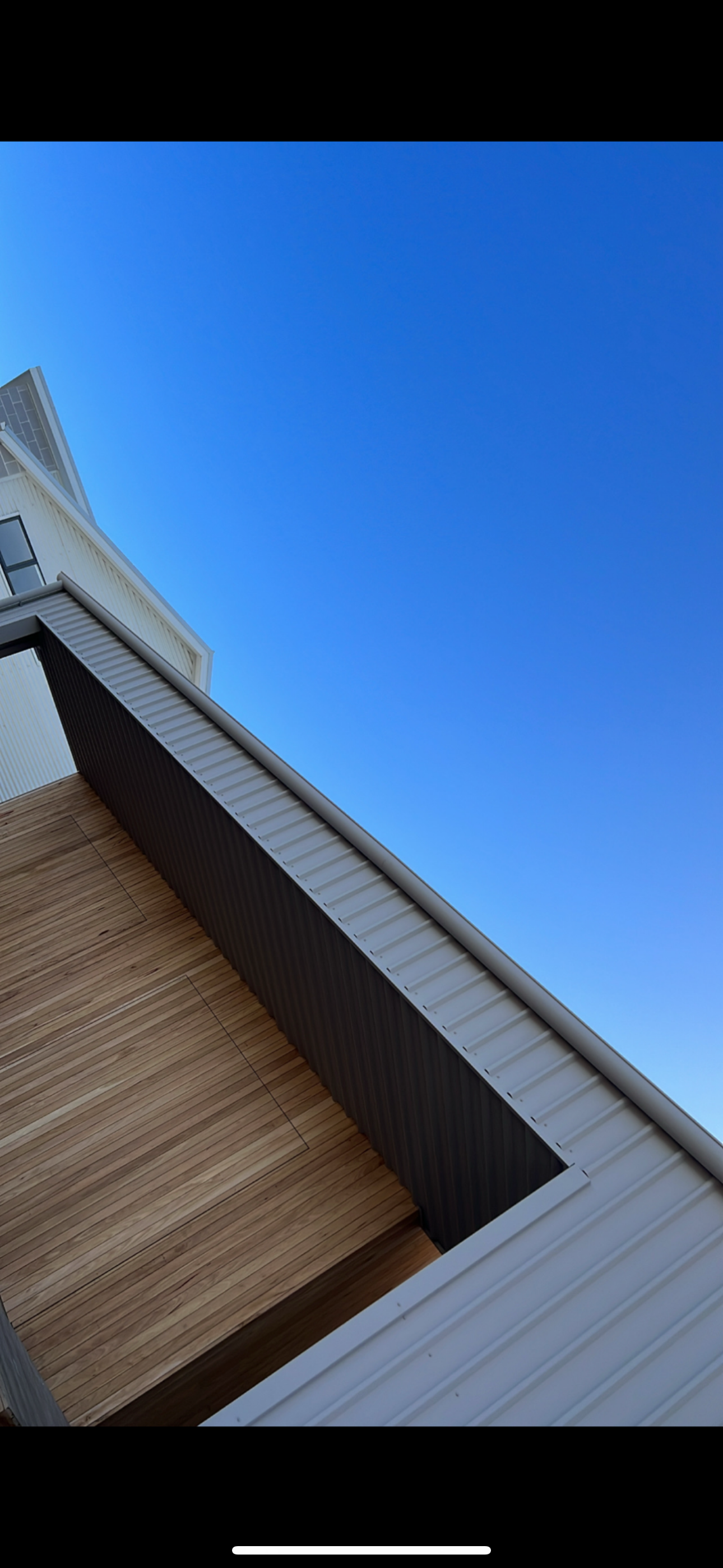 Part of a modern building with premium cladding, and a clear blue sky with a small section of another building with solar panels in the top left corner.
