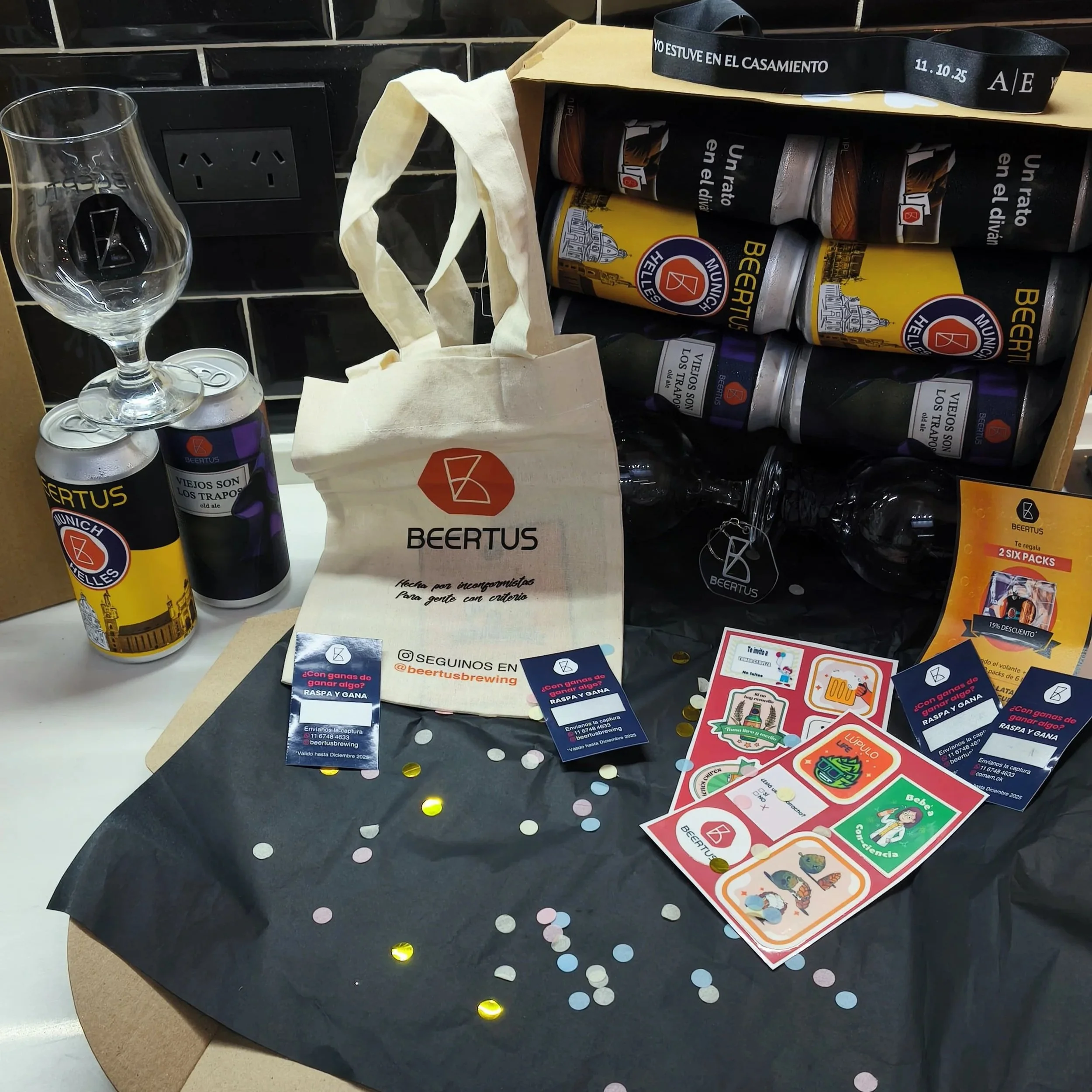 Decoraciones de celebración con una bolsa de tela de BEERTUS, latas de cerveza, tarjetas de juegos y confeti en una mesa.