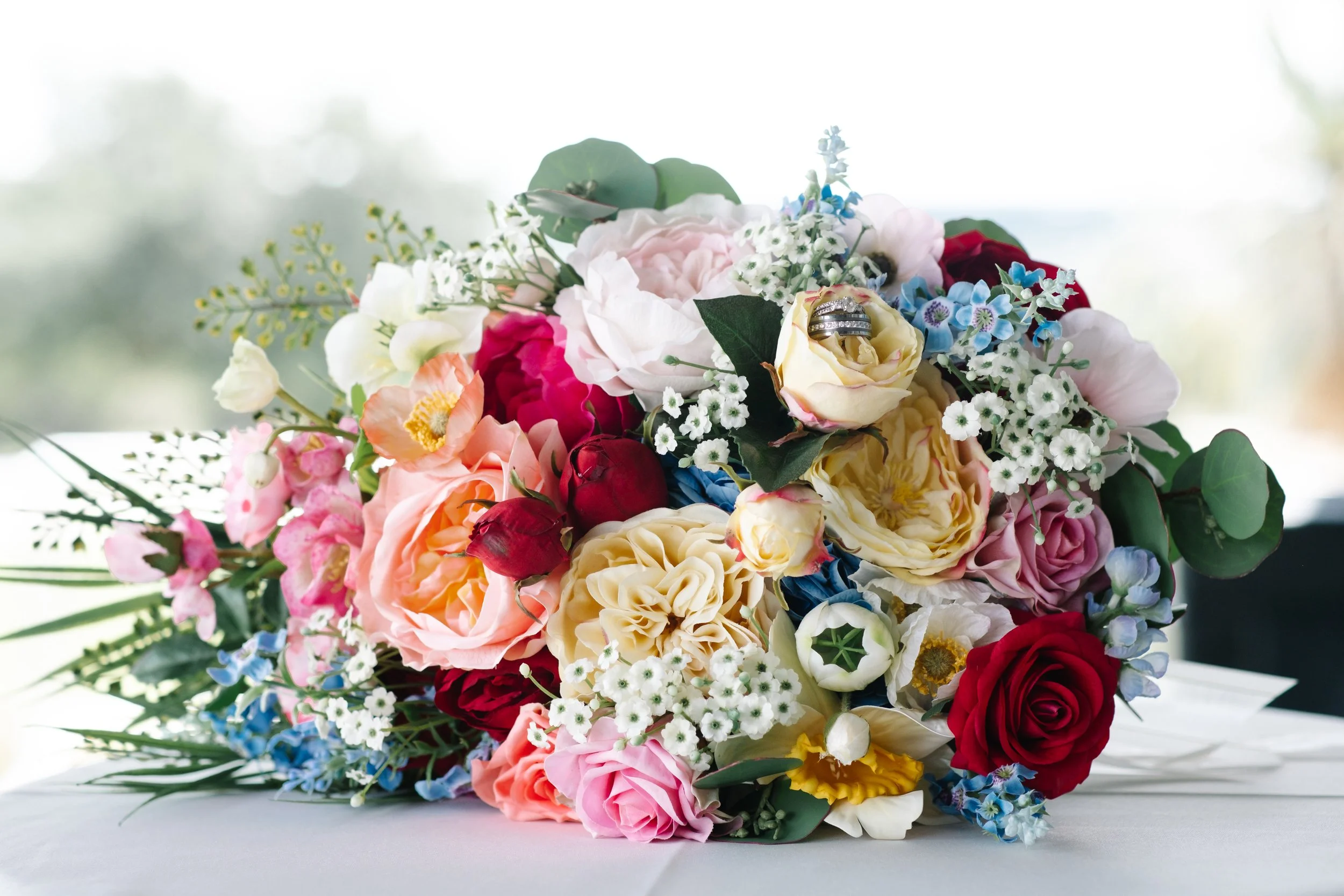 Colorful bouquet of various flowers with wedding rings placed on a white rose