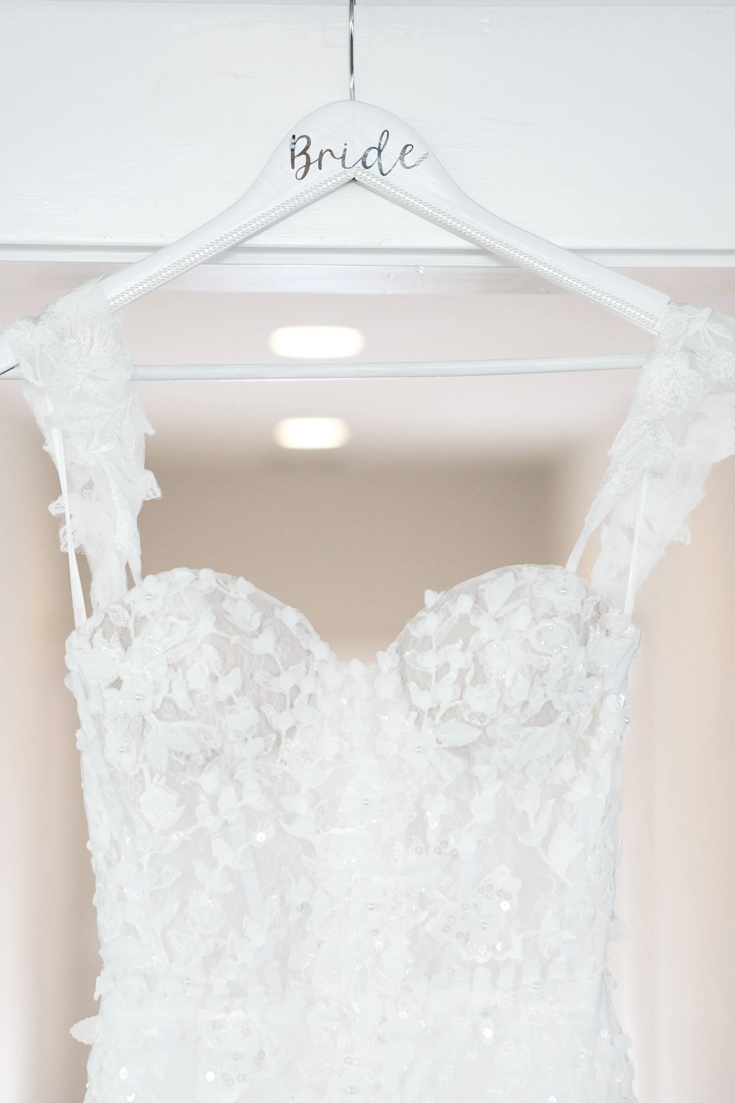 Wedding dress hanging on a white hanger labeled 'Bride' with lace details and floral embellishments.