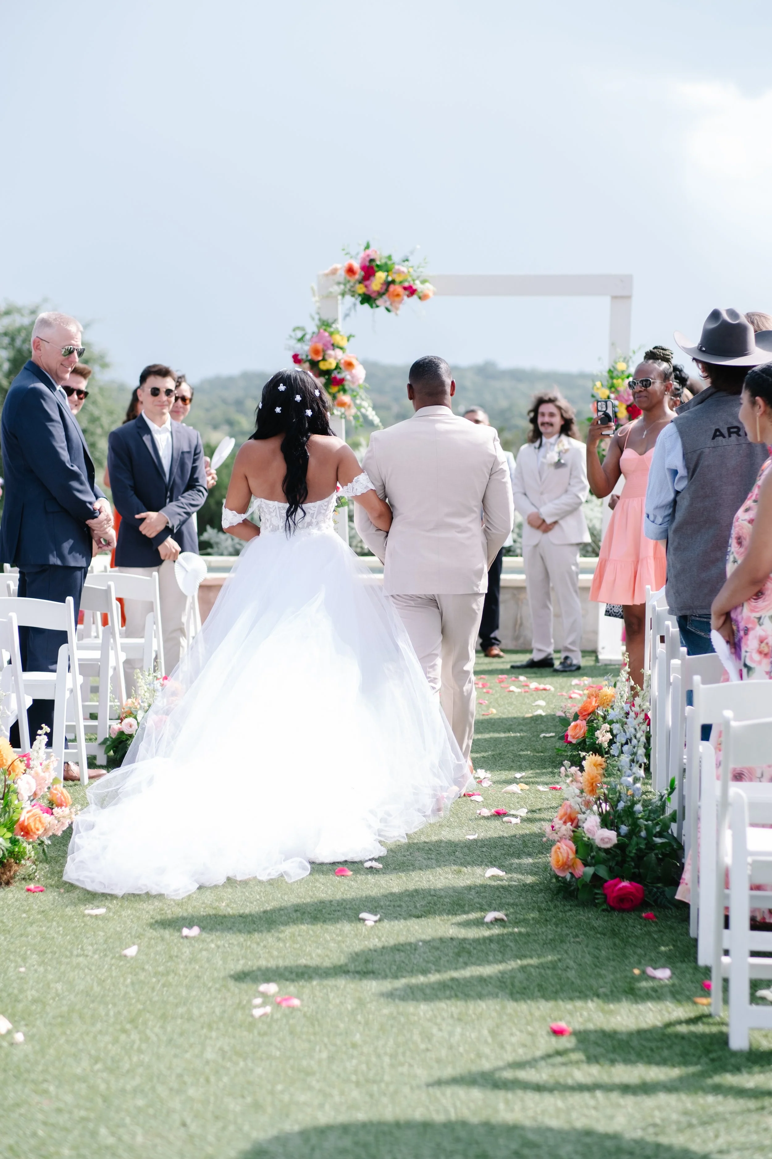 Bride and groom walking down the aisle during their outdoor wedding ceremony, with guests on either side and decorated with colorful flowers.