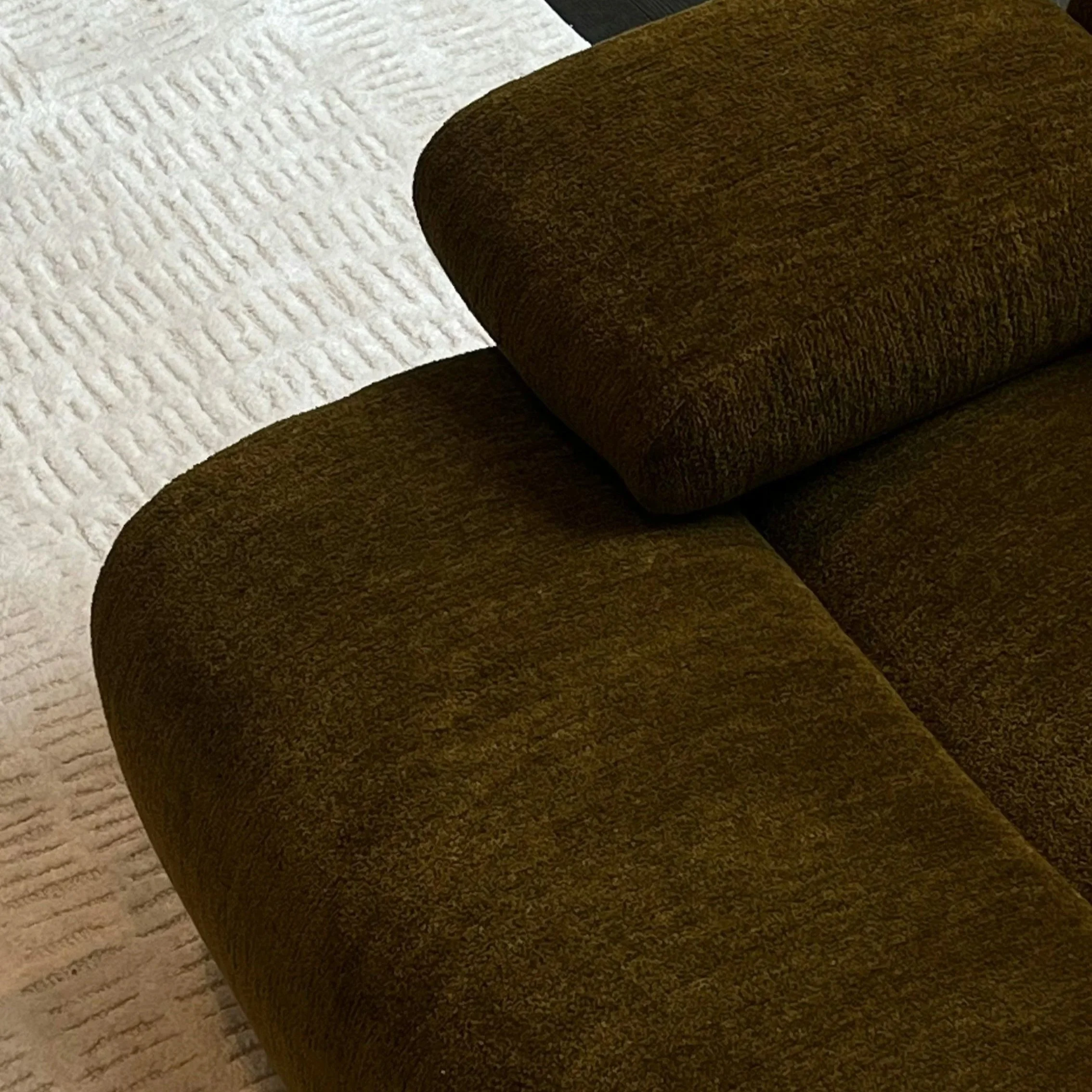Close-up view of a brown upholstered sofa on a white textured carpet.