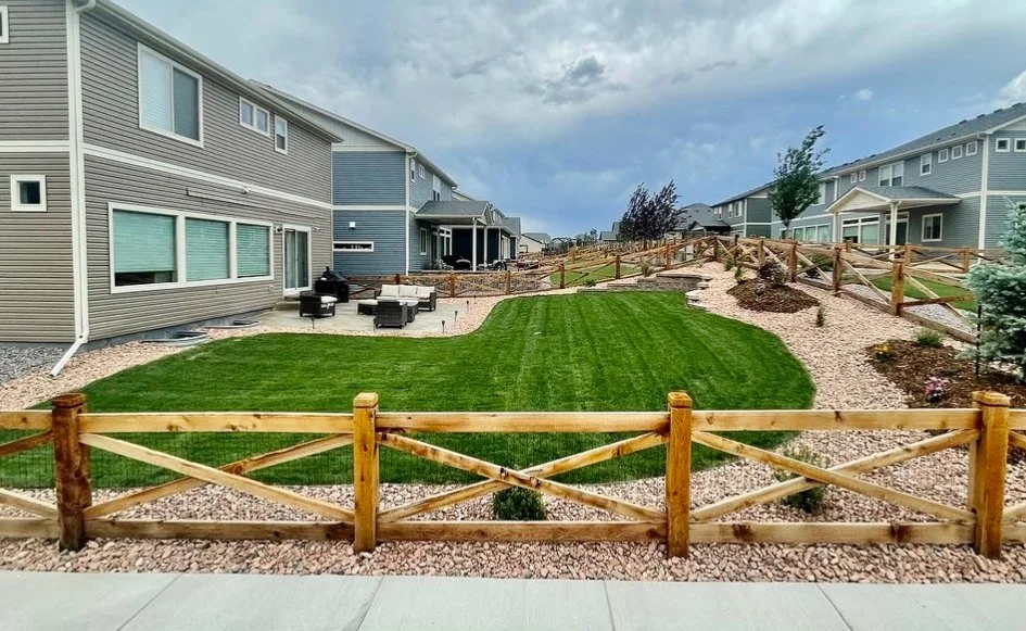Backyard with well-maintained green lawn, surrounded by a wooden fence and neighboring houses, under a cloudy sky.
