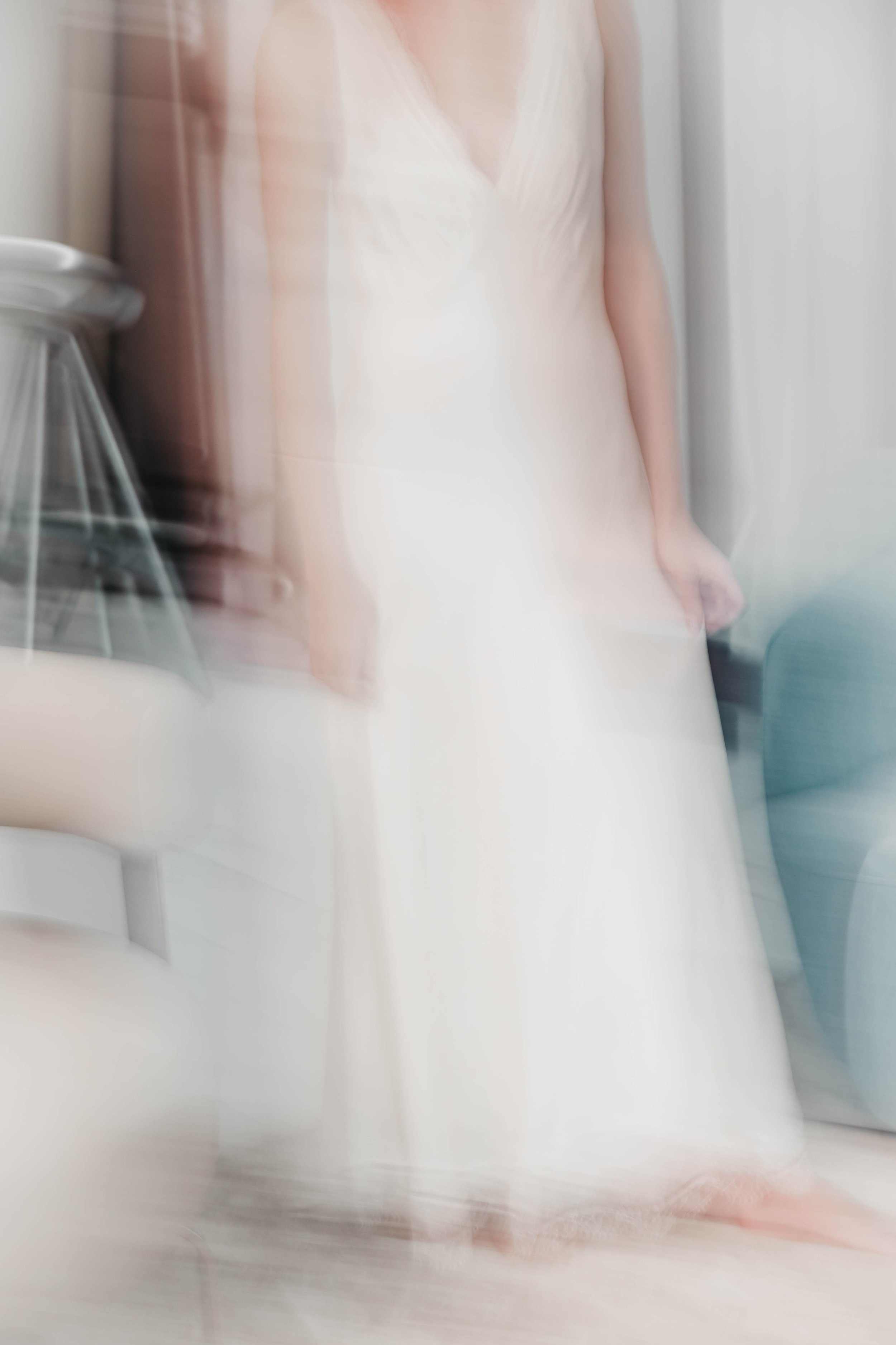 Blurred image of a woman in a white dress, standing indoors.