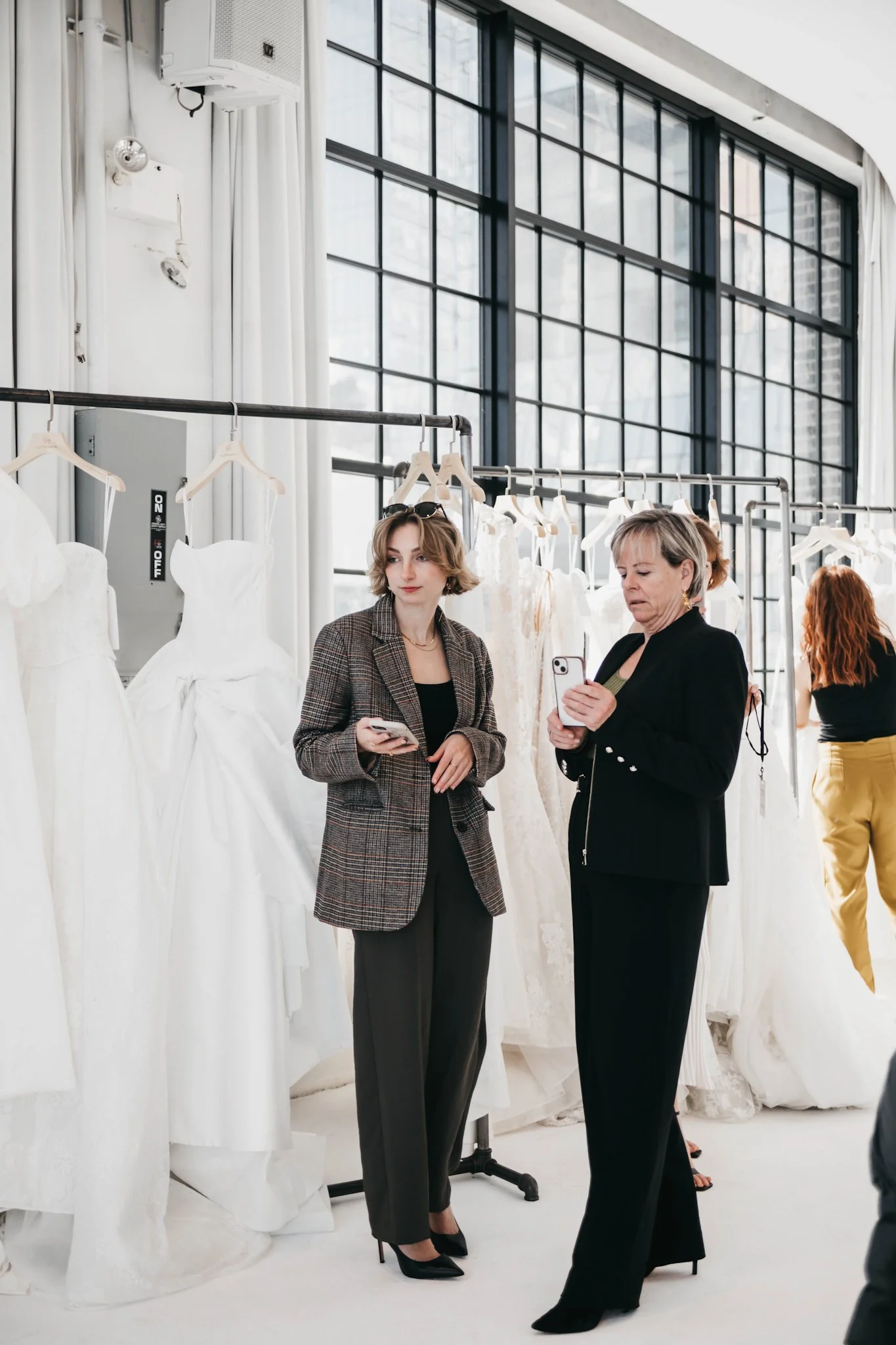 Women shopping for wedding dresses in a bright, modern bridal boutique, examining white wedding gowns on display.