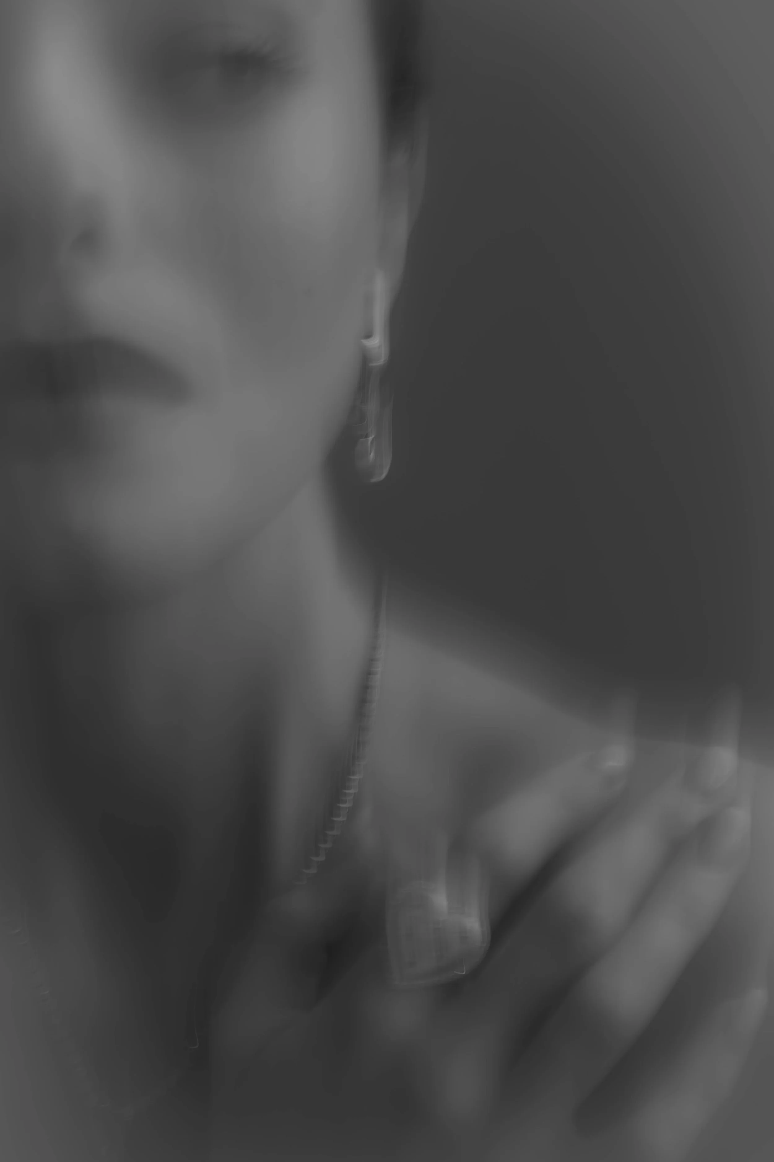 Close-up of blurred face of a woman with drop earrings, in black and white.