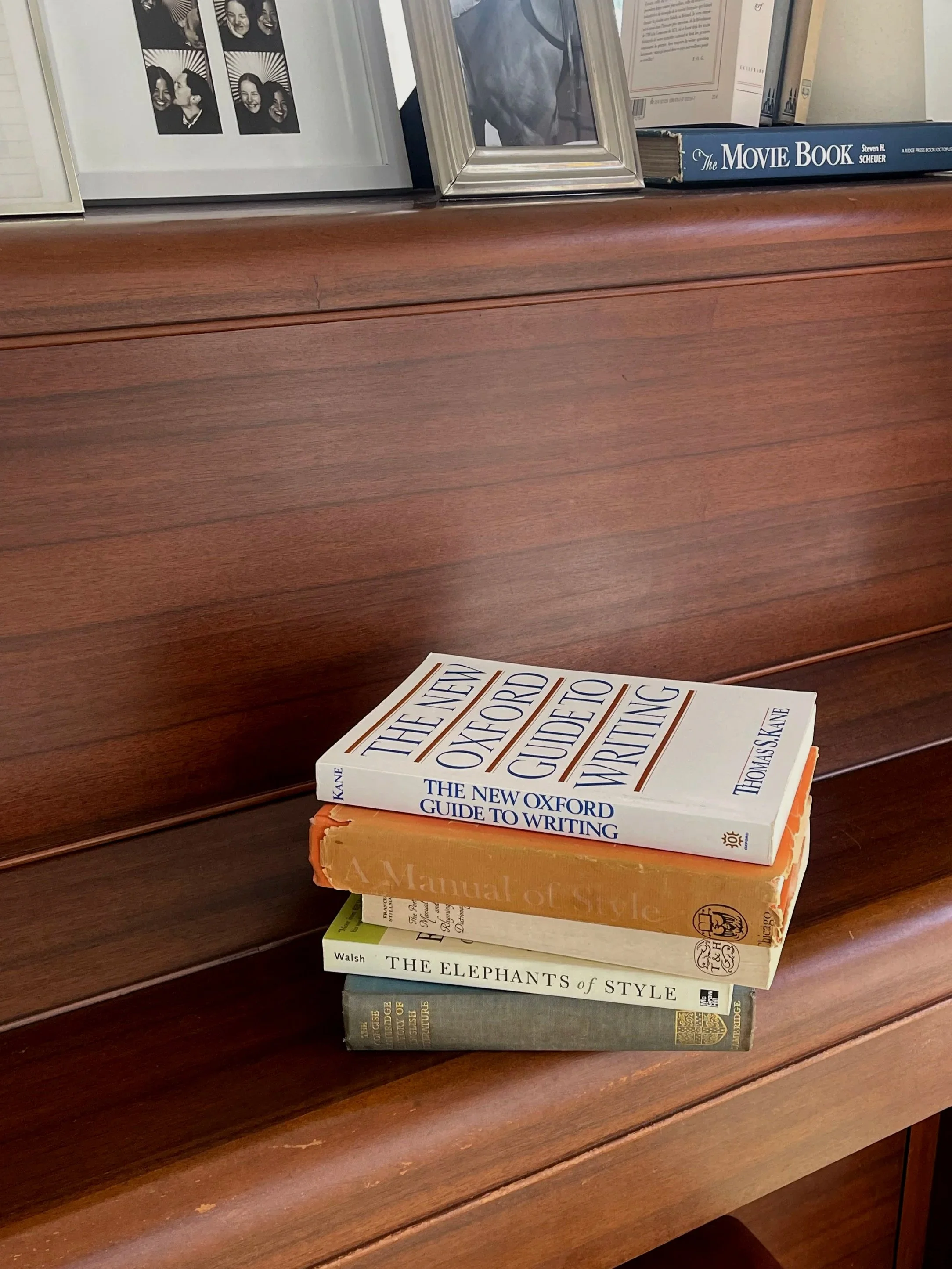 Stack of four books on a wooden surface, with some framed photographs and a book titled 'The Movie Book' in the background.