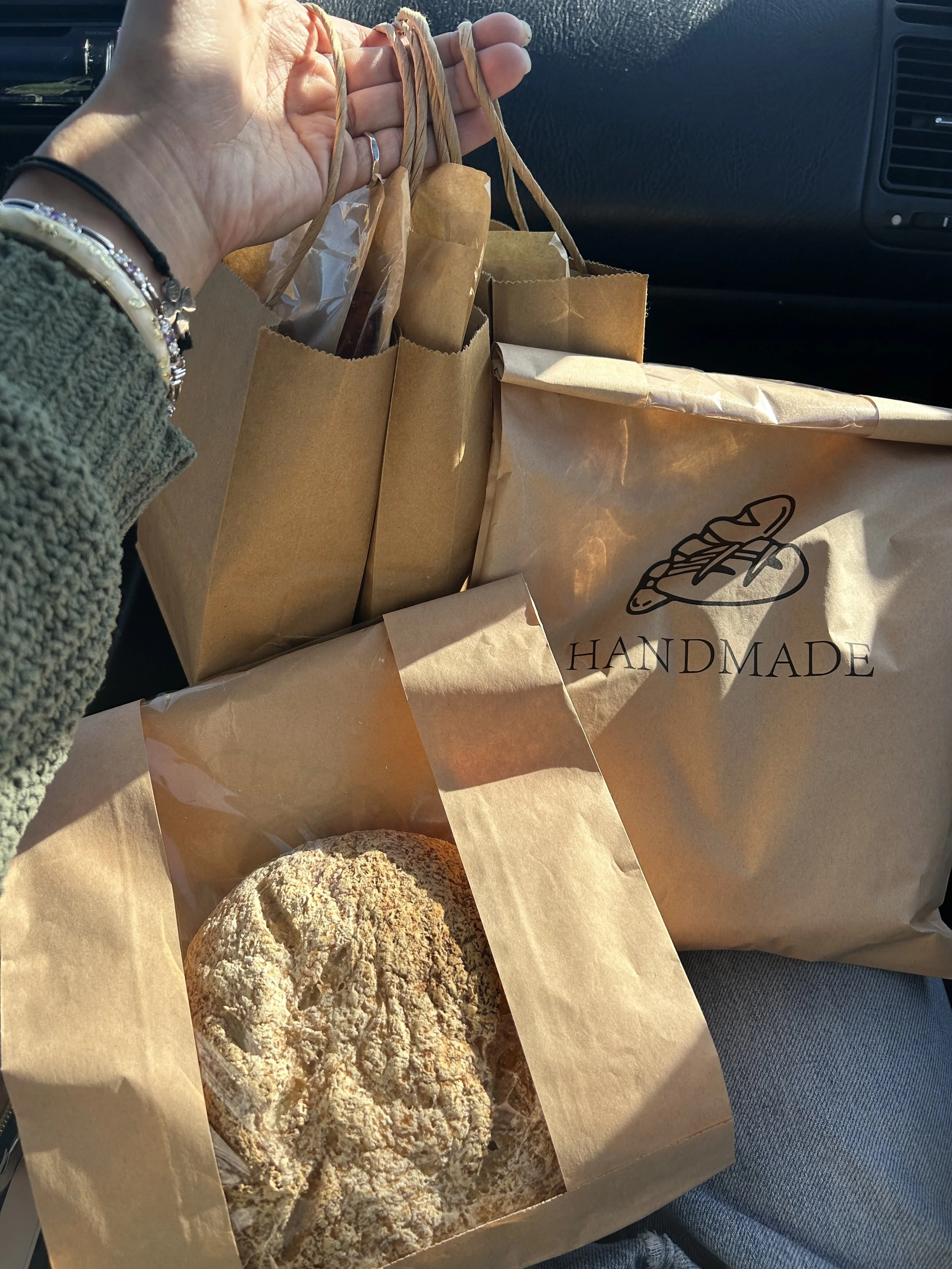 Photo of packaged bread, front and back. Small bags of cookies in background held up by a hand.