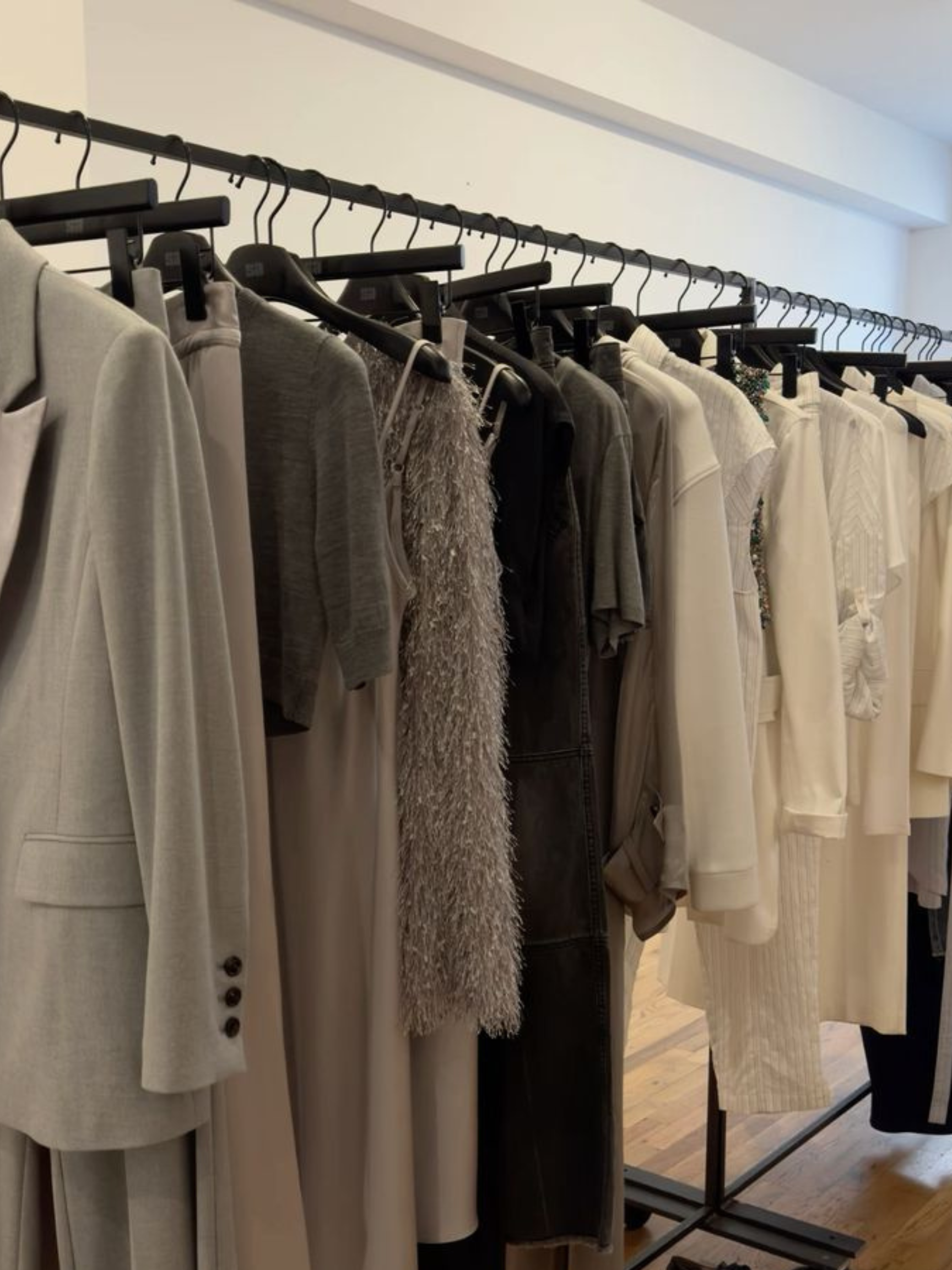 Clothing rack with various garments including blazers, dresses, and tops in neutral and dark colors.