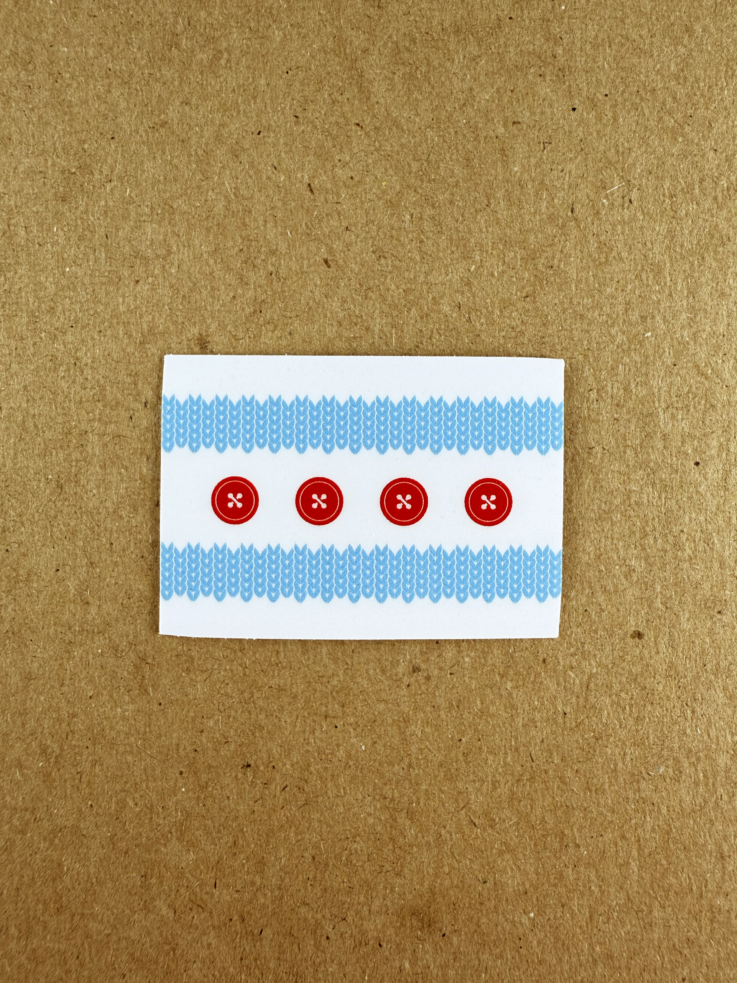 A sticker representing the Chicago city flag with four red buttons arranged horizontally in the center, decorated with blue knitted pattern borders at the top and bottom, placed on a brown background.
