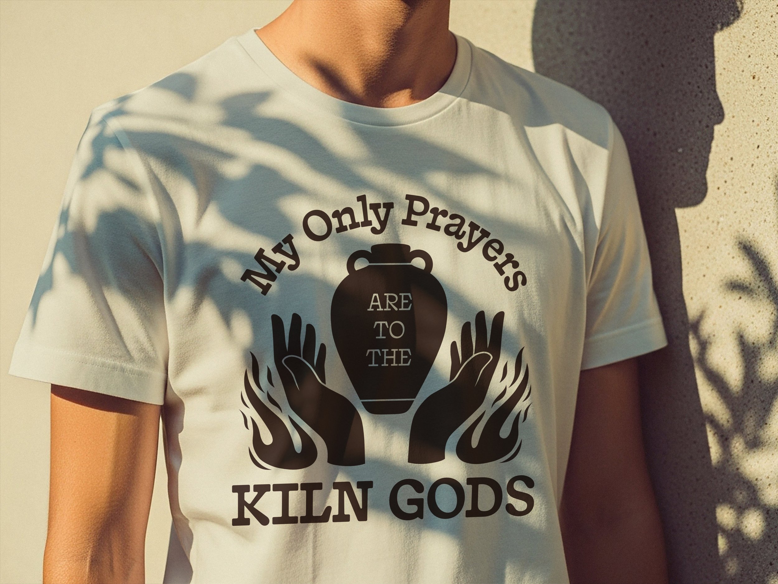 Cropped image of a man wearing an off-white t-shirt that says "My Only Prayers are to the Kiln Gods"