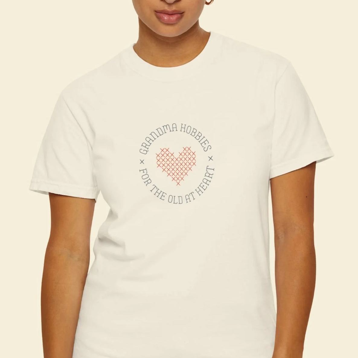 A white T-shirt with a cross-stitched red heart design and the text 'Grandma Hobbies for the Old at Heart' around it.