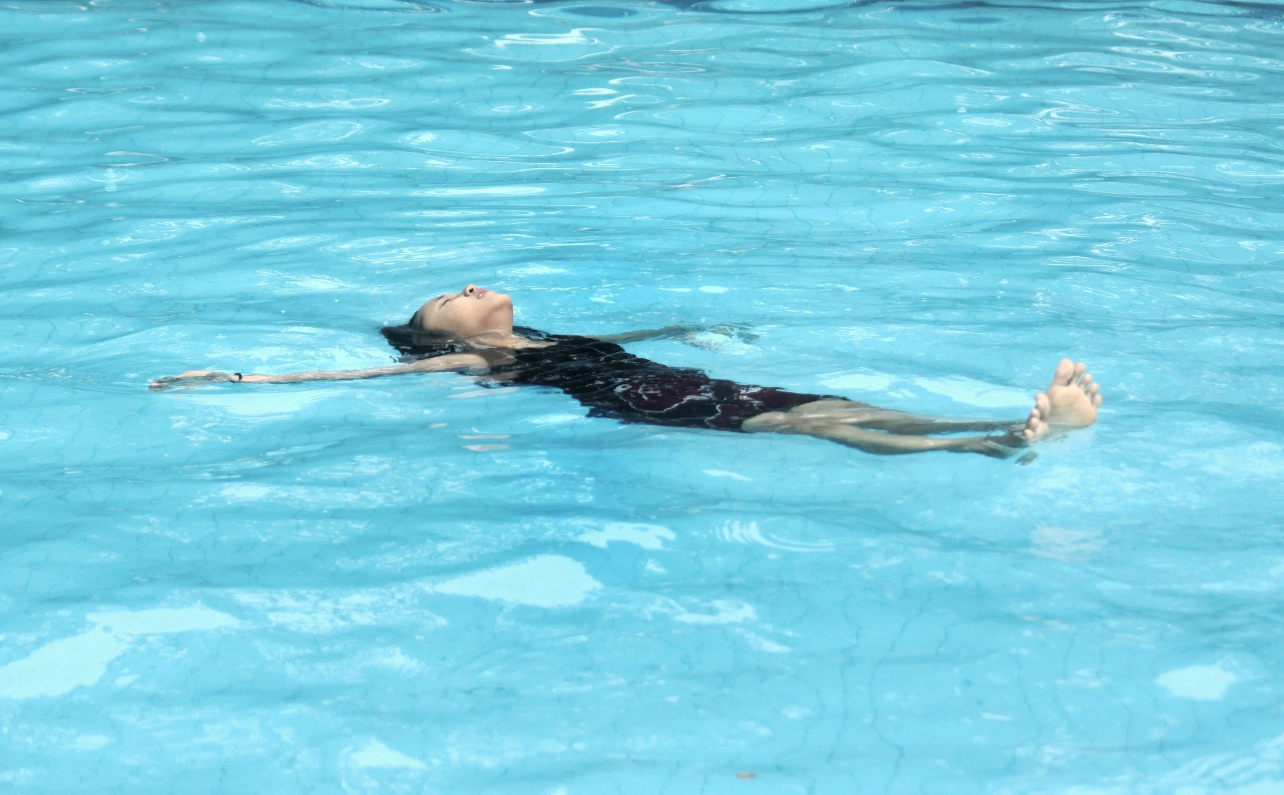 A woman floating on her back in a swimming pool with clear blue water