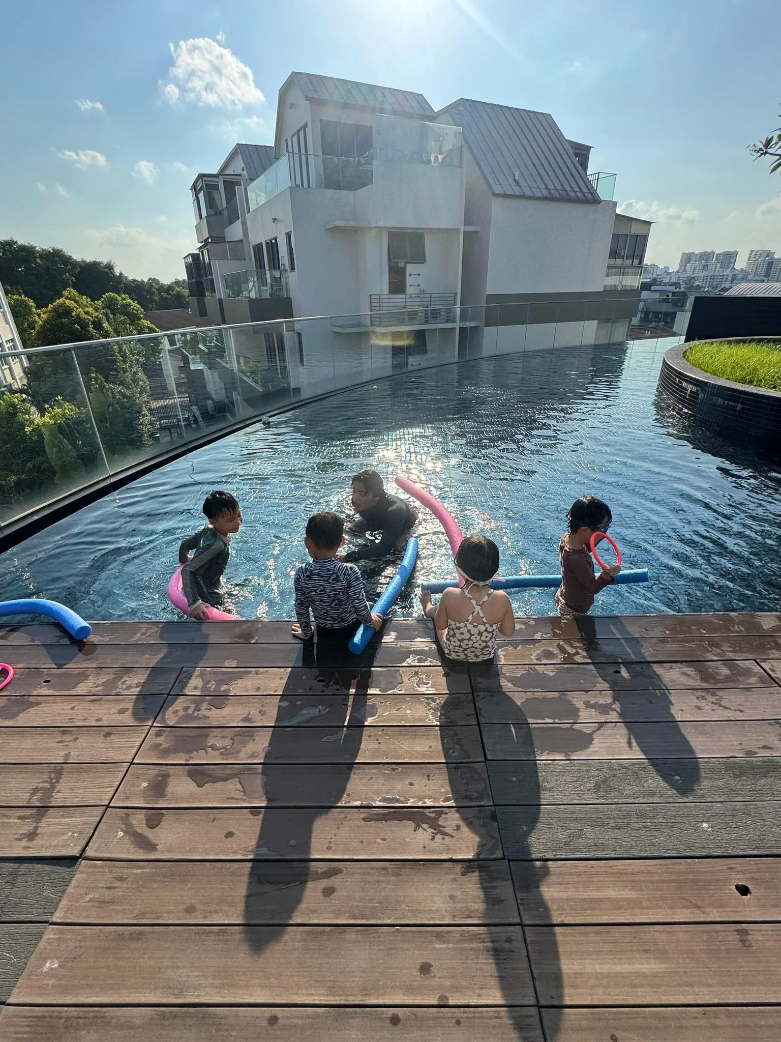 Children in swimsuits playing in an infinity pool on a rooftop during daytime.