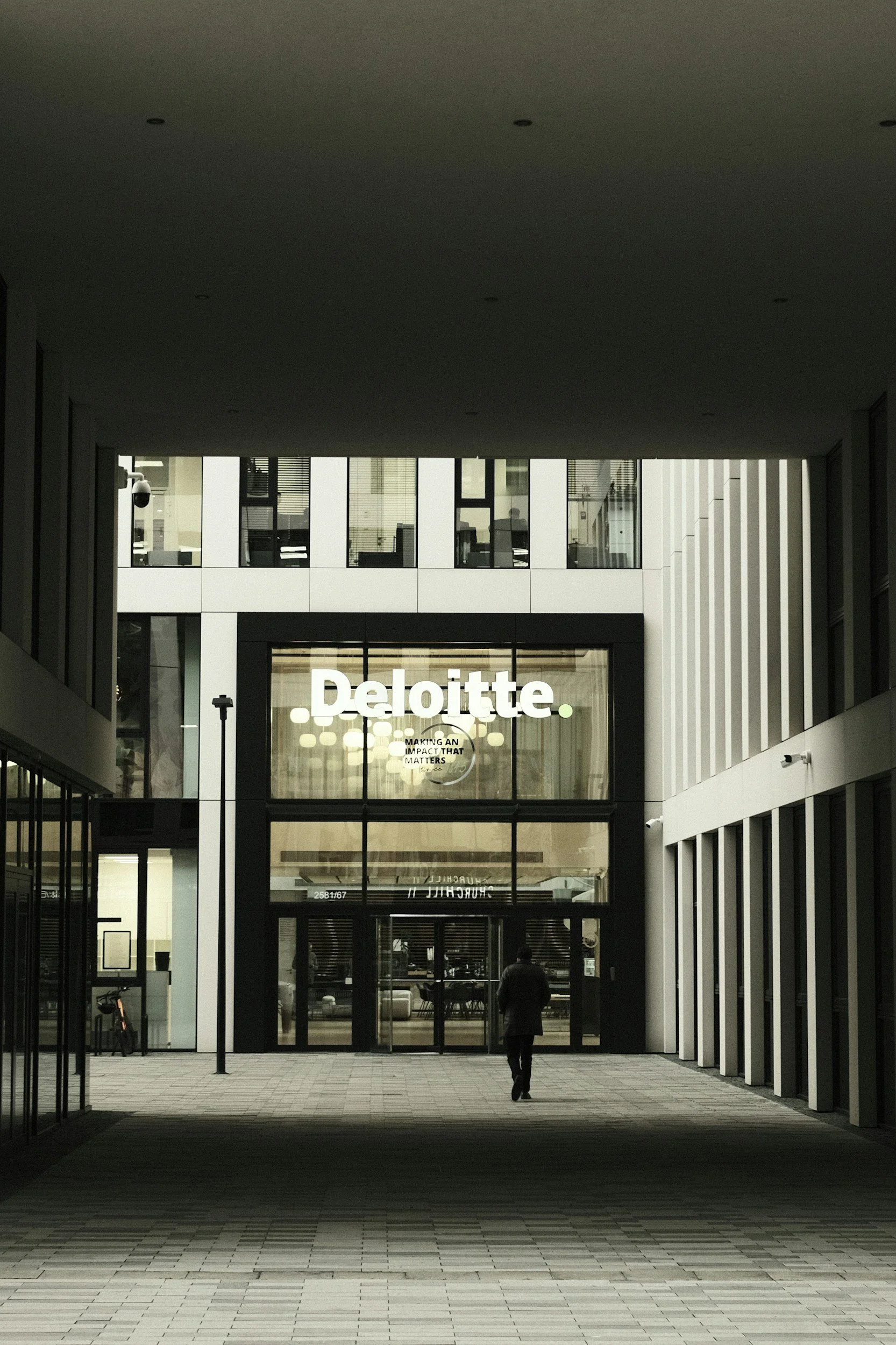 A modern, high-rise corporate office building with a sleek glass architecture, representing enterprise digital systems and global professional services consulting for Deloitte.