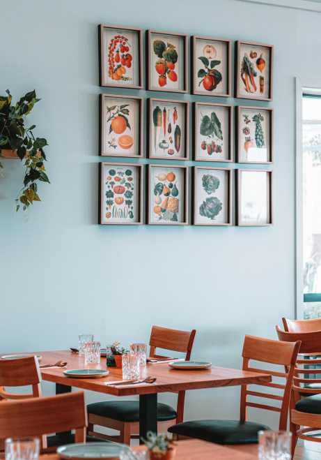Interior dining room of Copia restaurant in Orakei showing wooden tables and a gallery wall of framed botanical illustrations, featured in Verve Magazine.
