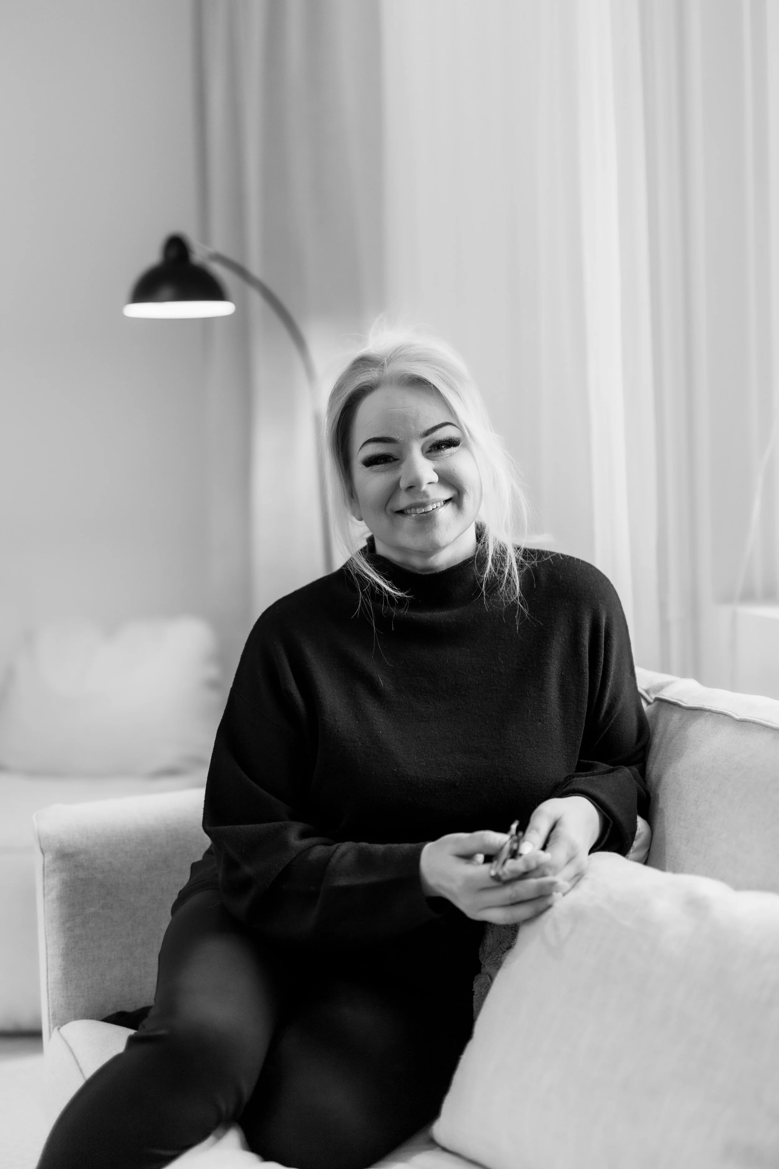 Valkoinen nainen hymyilee istuessaan sohvalla kotona.