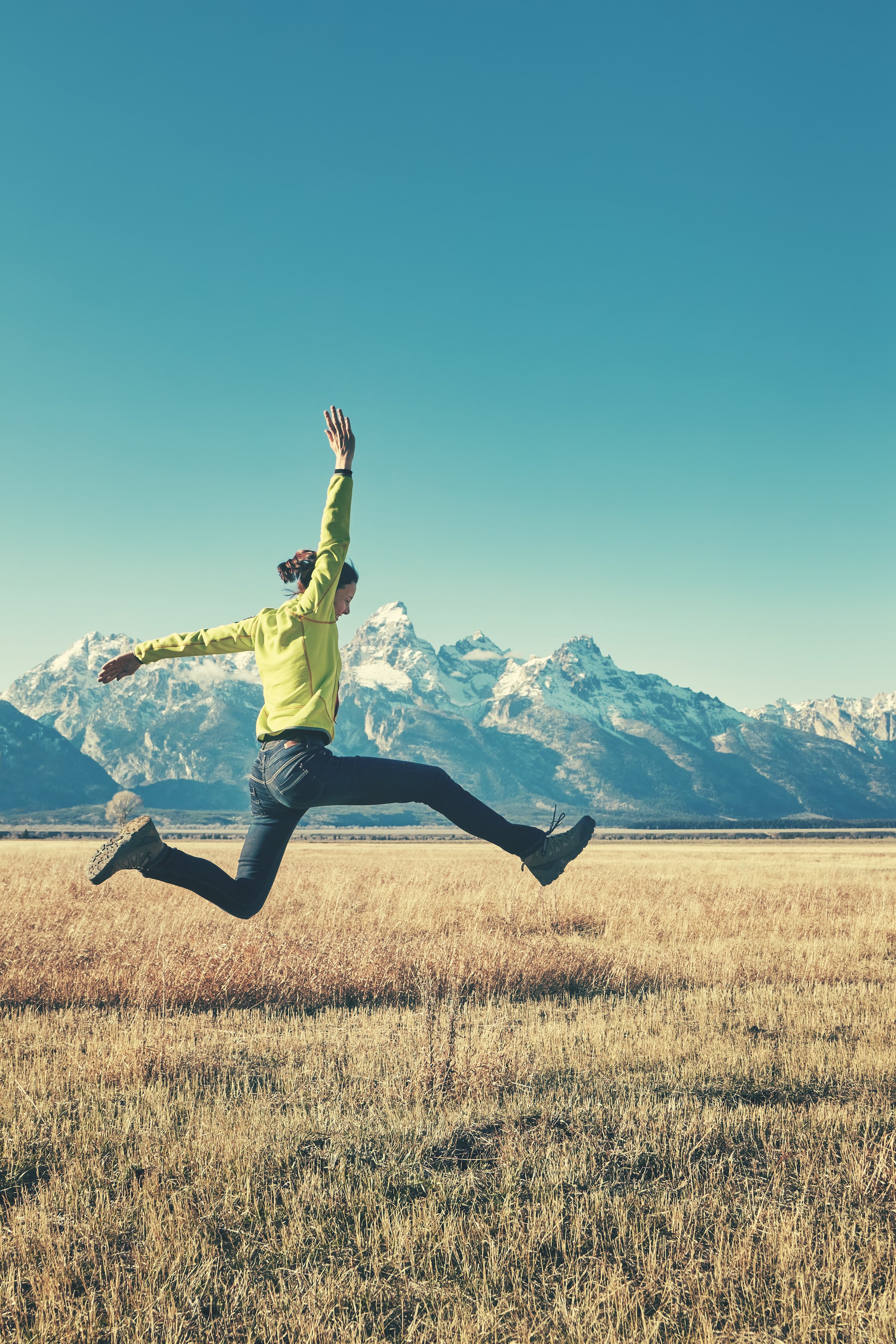 A woman jumping in a grassy field with mountains in the background