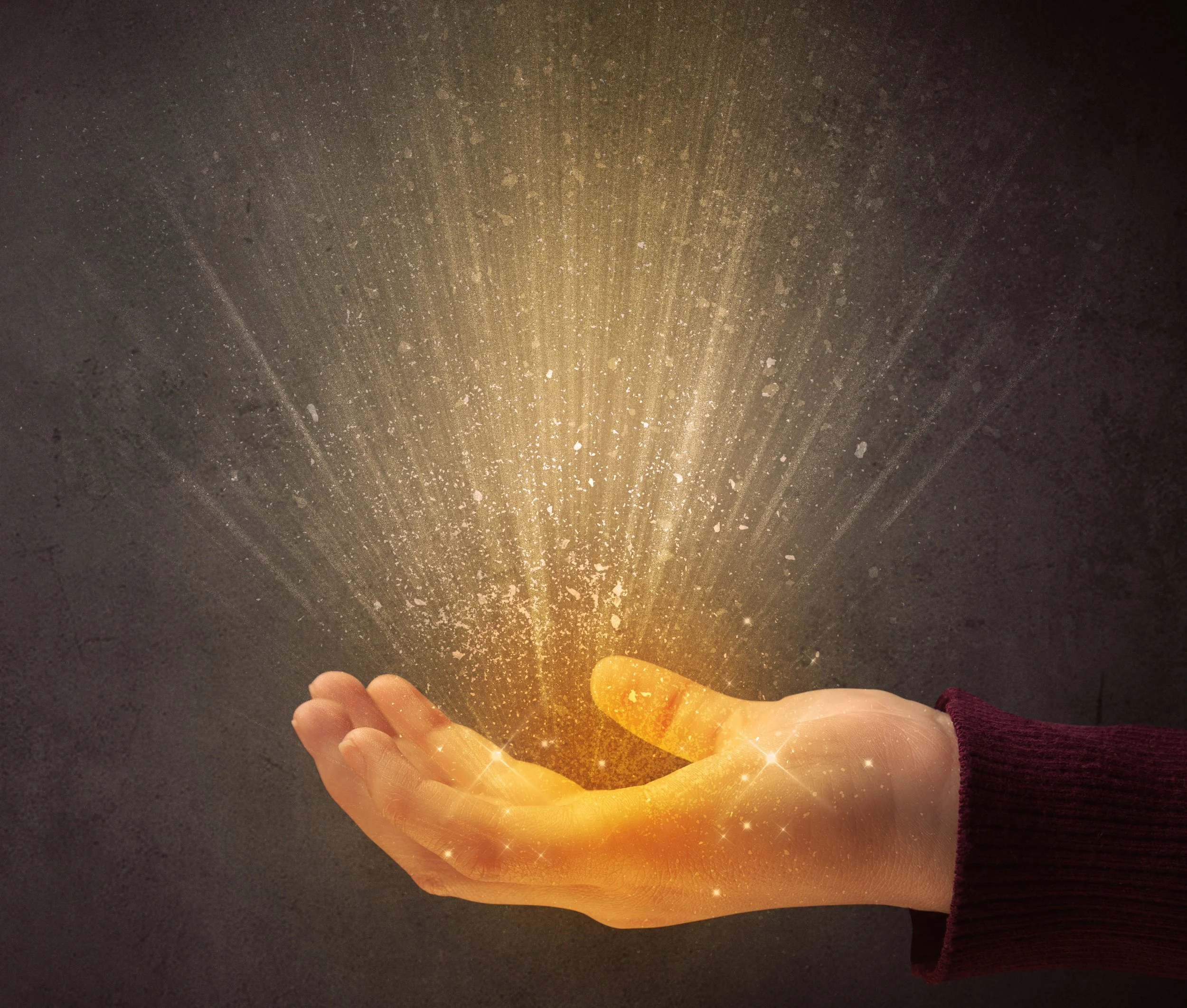 A person holding a glowing, sparkling, golden object in their hand, with light rays and sparkles emanating from it against a dark background.