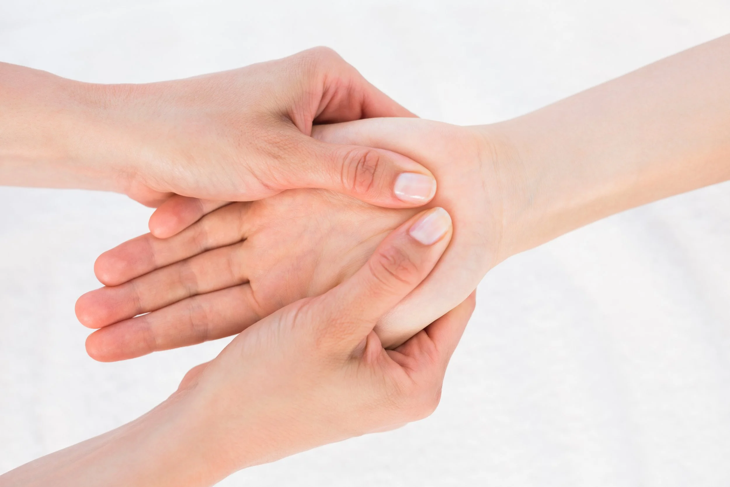 Close-up of two hands engaging in a gentle hand massage or therapy, with a plain white background.