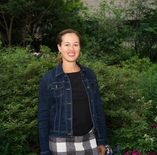 hilary kopple, anxiety therapist ny, wearing denim coat, black shirt, plaid skirt in front of a bush