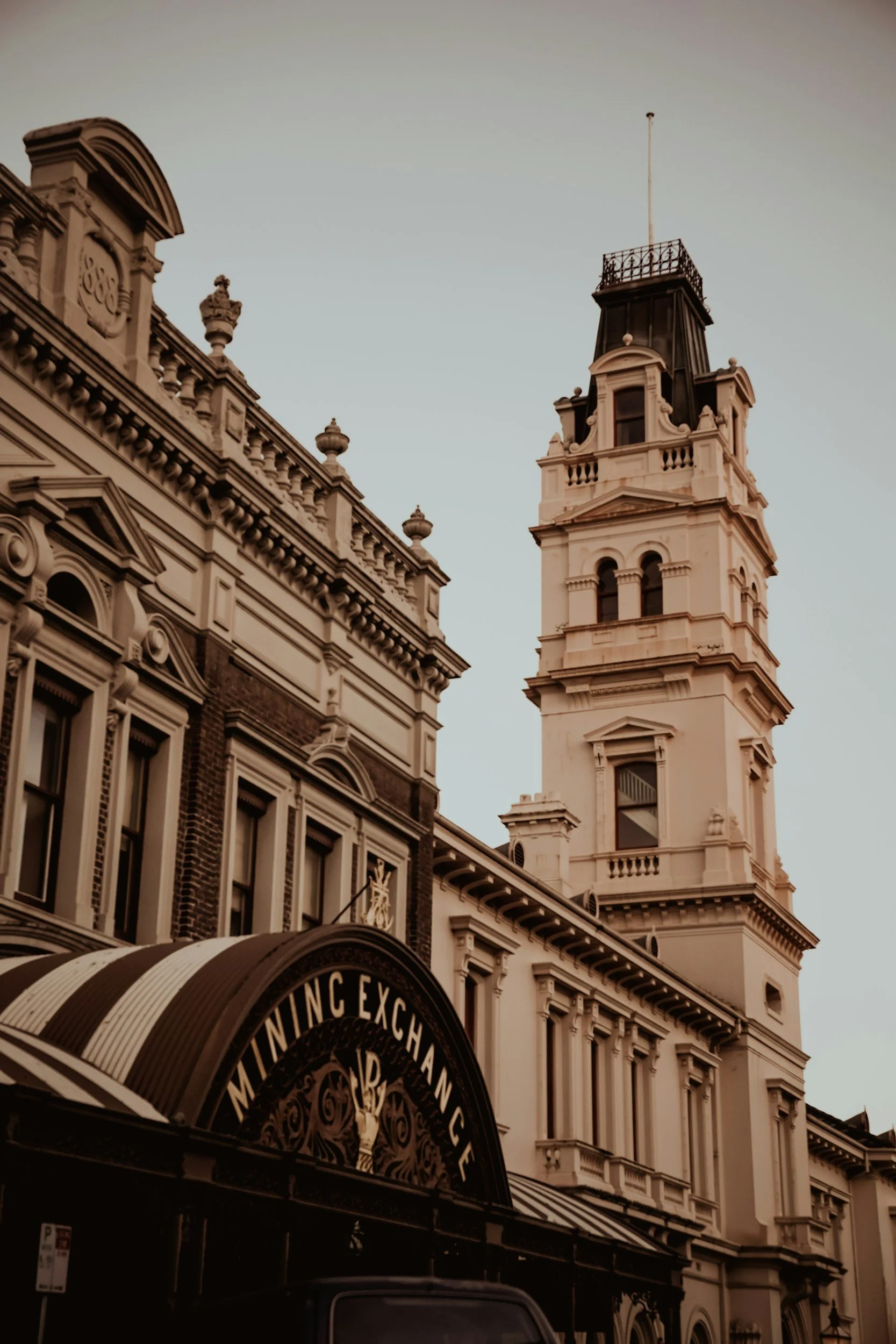 Historic building with ornate architectural details and a tall clock tower, part of a shopping arcade with a curved awning.