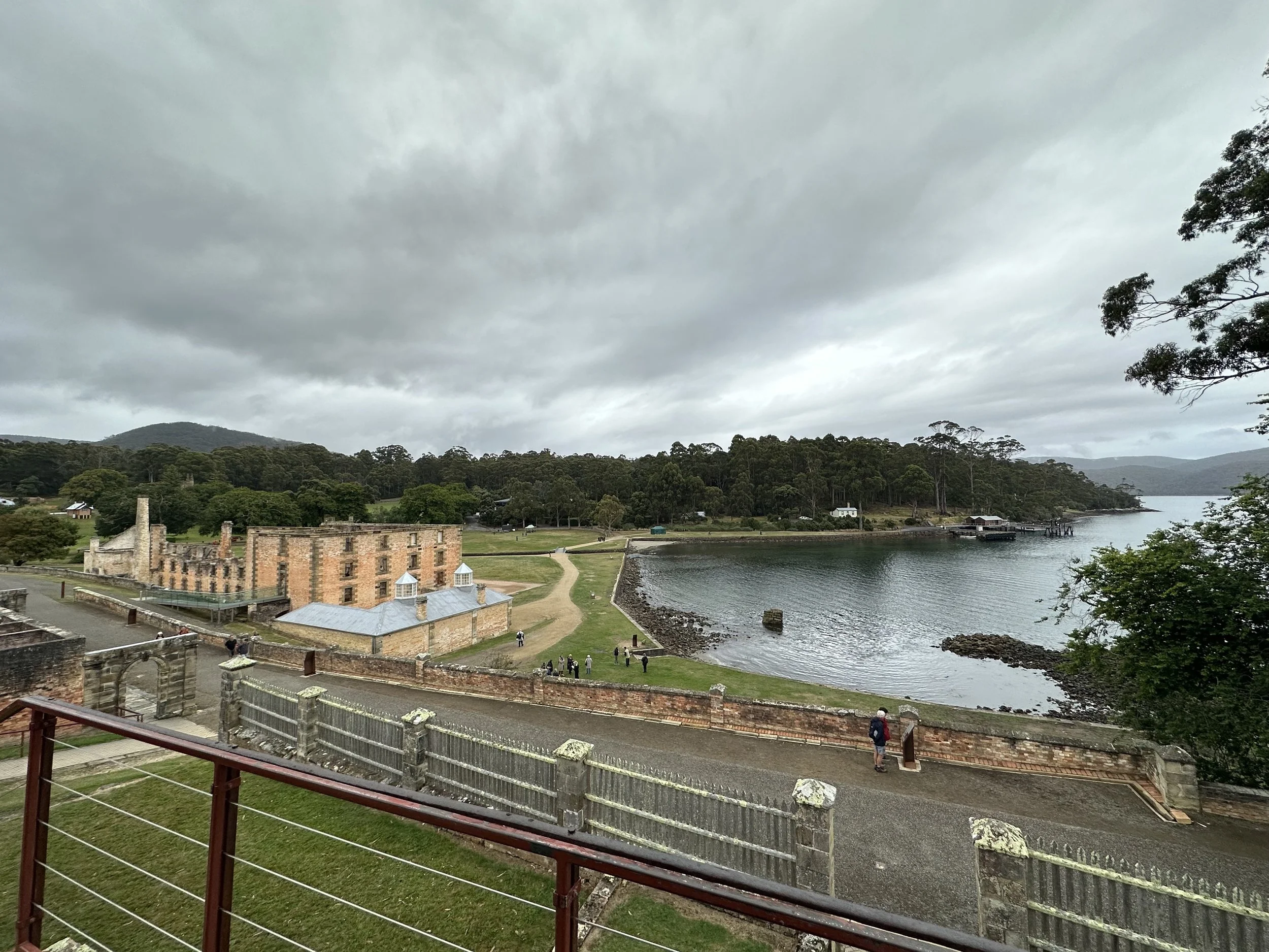 View of historic brick building and surrounding landscape with trees, water, and overcast sky.