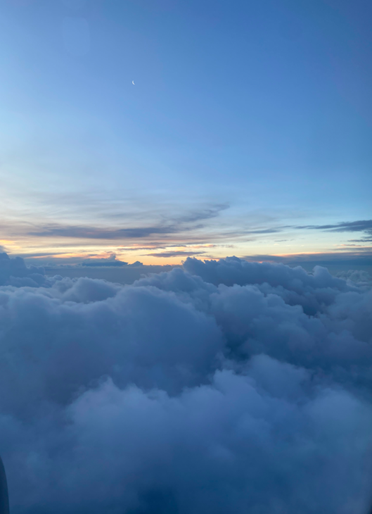 View of sky with clouds and a crescent moon during sunset or sunrise.