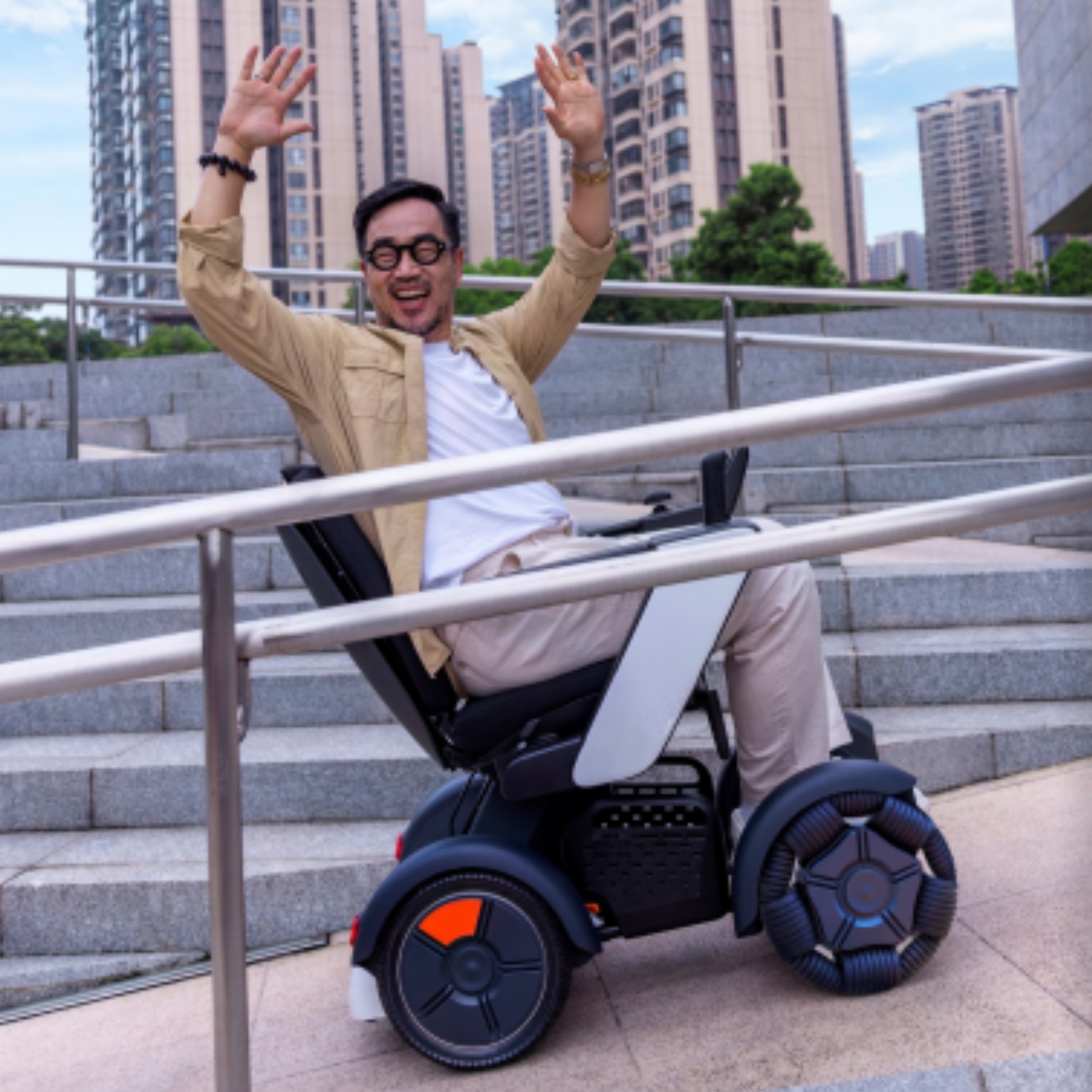 Man in an electric wheelchair celebrating outdoors on city steps with buildings in the background.