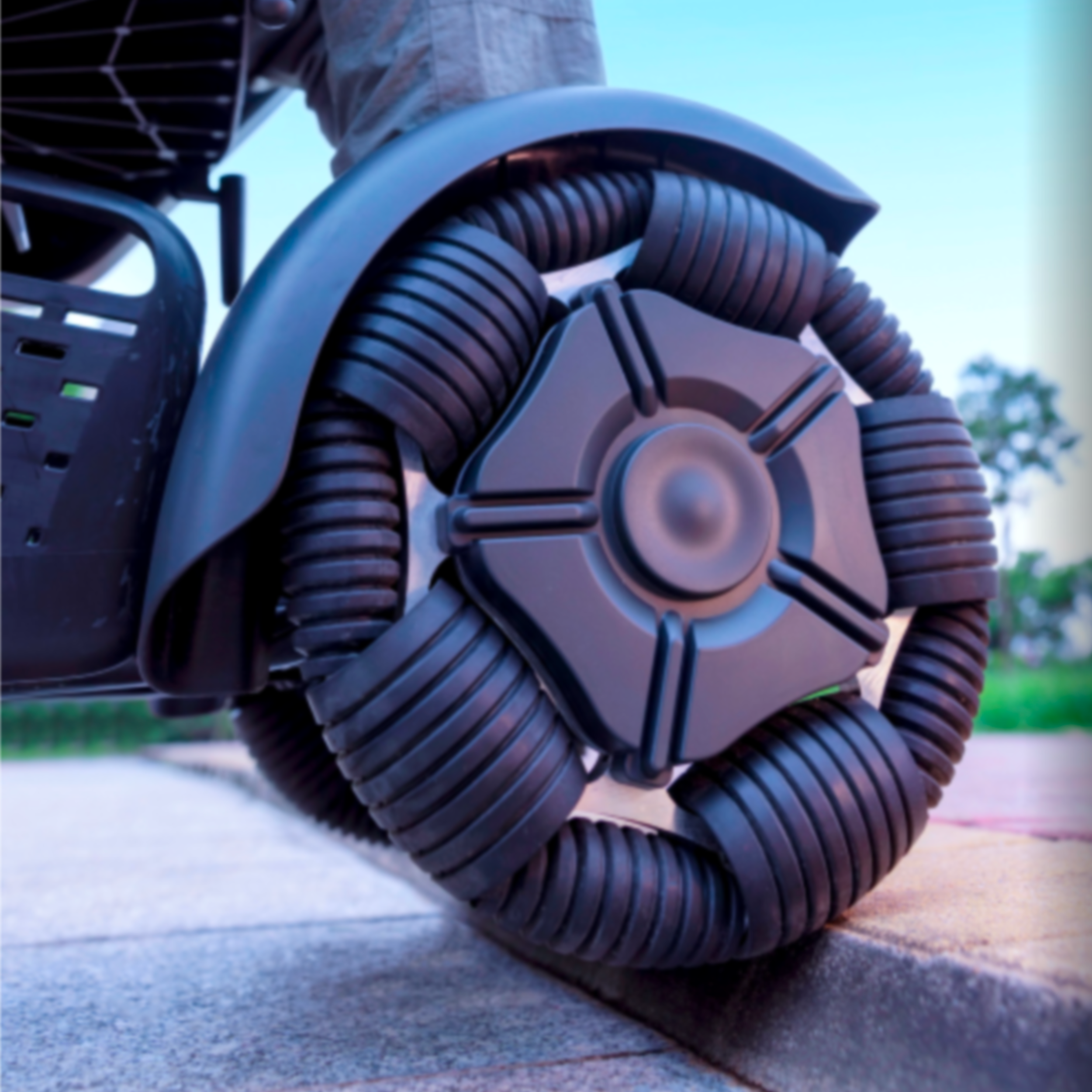 Close-up of a futuristic robotic wheel with multiple black, flexible segments and a central circular component, outdoors on a paved surface.