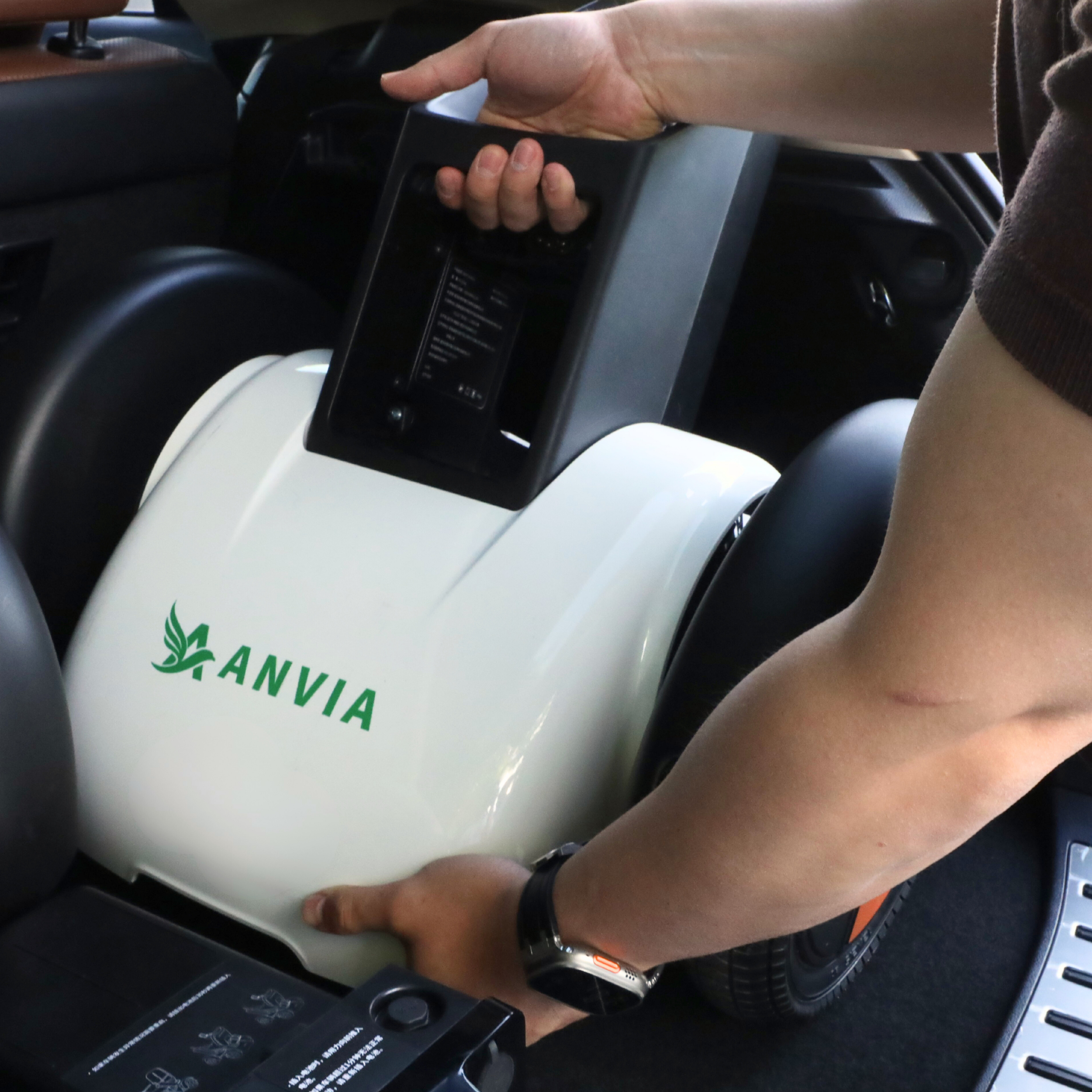 A person is handling an ANVIA brand device, which appears to be a portable air purifier or generator, inside a vehicle. The person is holding a remote or control panel, and a watch is visible on their wrist.