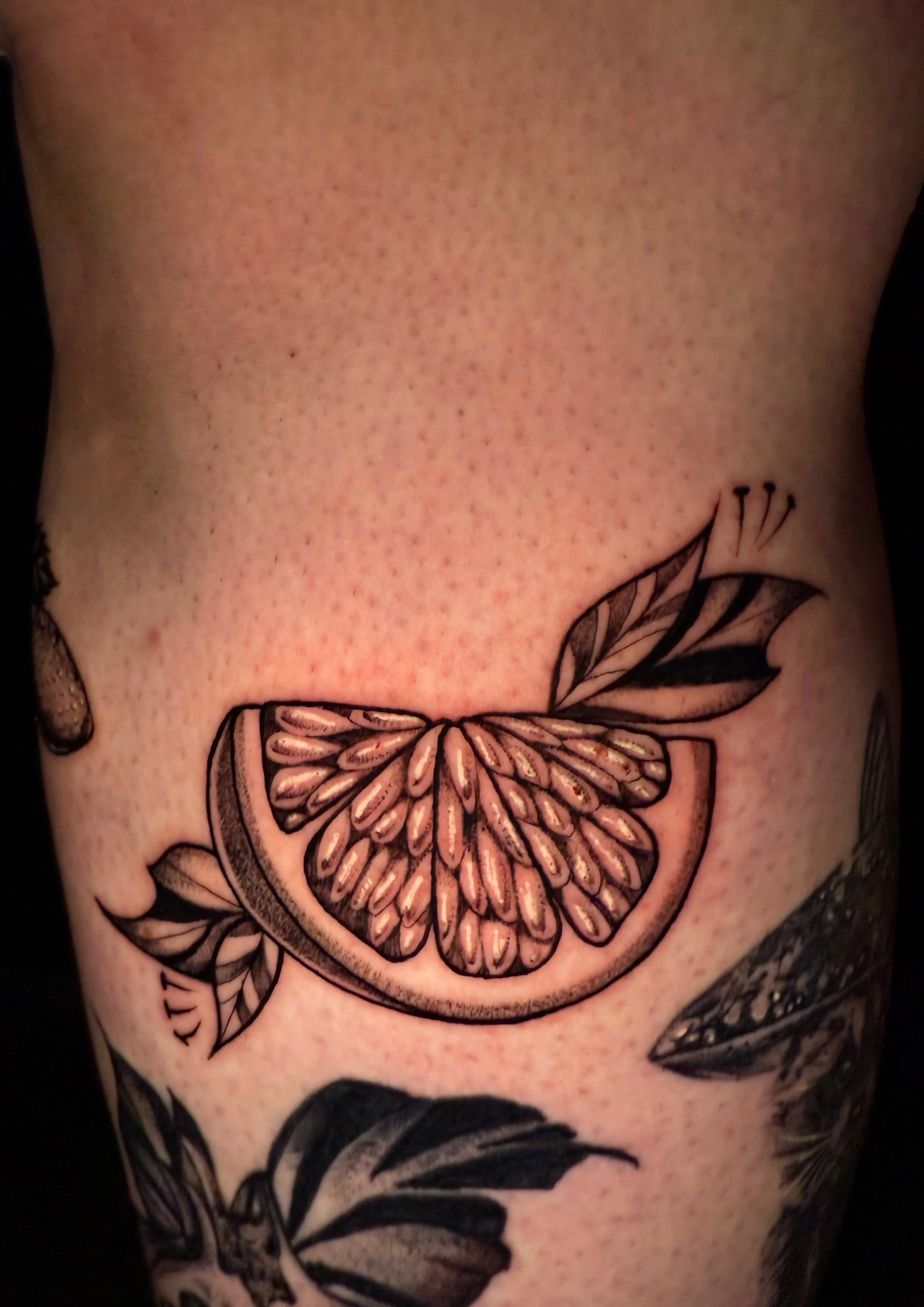 Tattoo einer Zitronenscheibe mit Blättern auf menschlicher Haut.