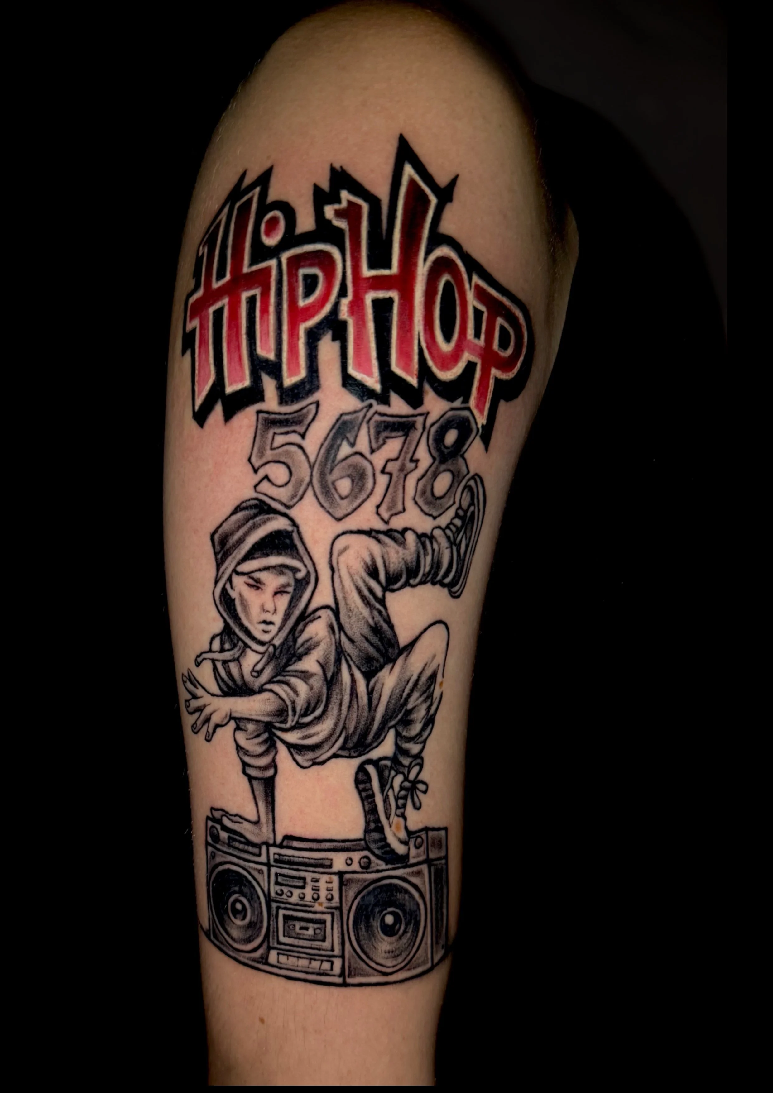Tattoo auf einem Arm, das den Text 'Hip Hop' in großen, roten Buchstaben mit schwarzen Umrissen zeigt. Darunter sind die Zahlen 5, 6, 7, 8. Es gibt eine Zeichnung eines Hip-Hop-Tänzers in einer dynamischen Pose auf einem DJ-Controller.