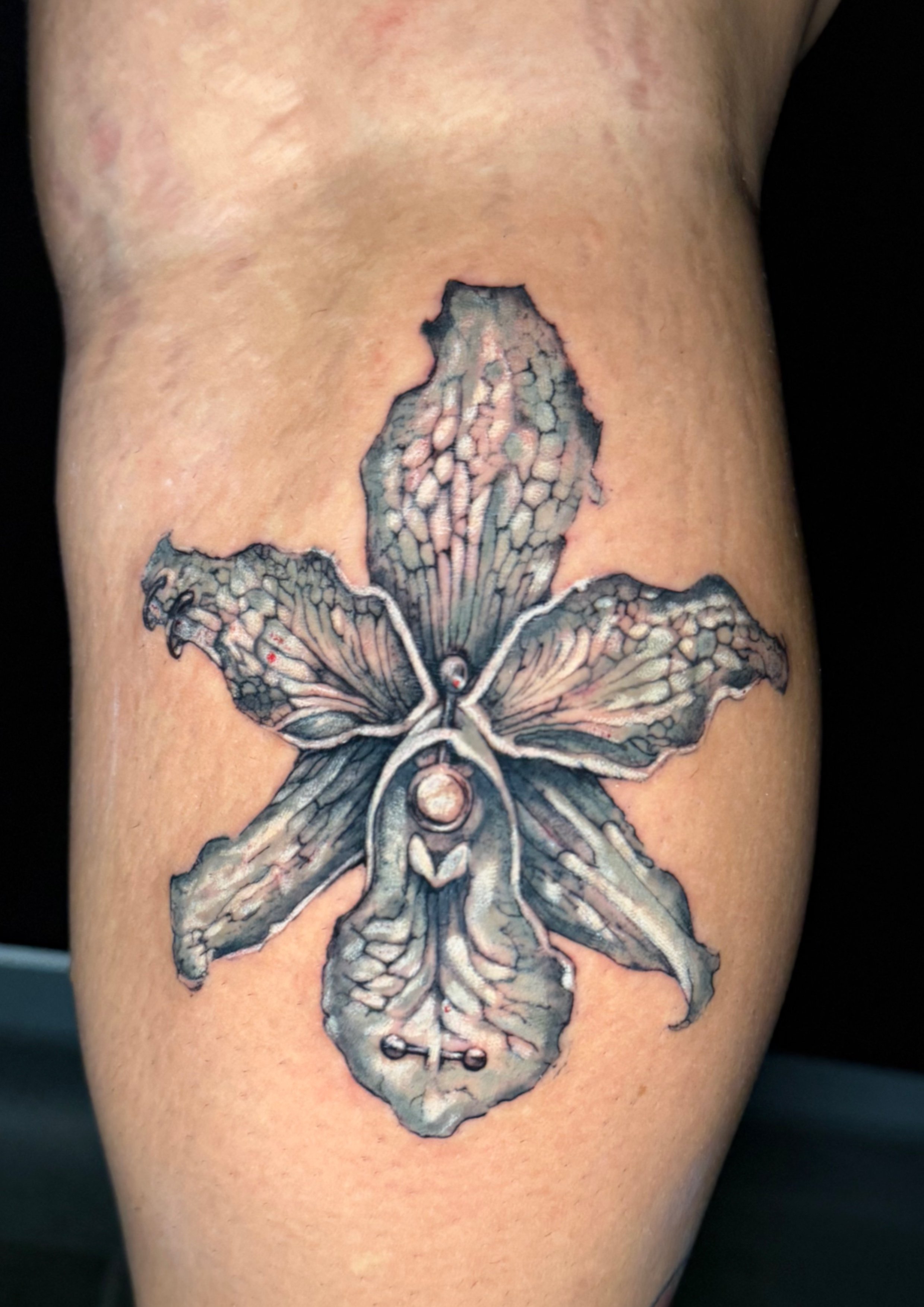 Tattoo einer Orchidee auf menschlicher Haut, detailliert in Schwarz, Grau und zarten Farbtönen.