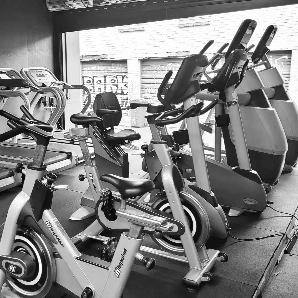 Indoor gym with exercise bikes, treadmills, and elliptical machines near a large window.