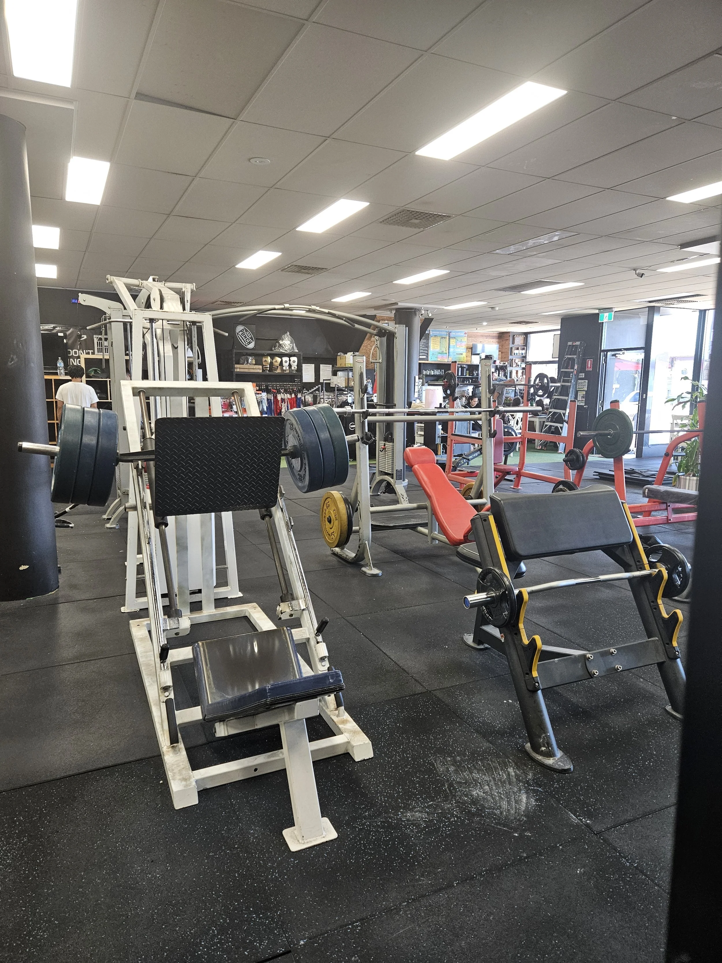Indoor gym with various weightlifting equipment, including benches, barbells, and weight plates, in a well-lit workout facility.