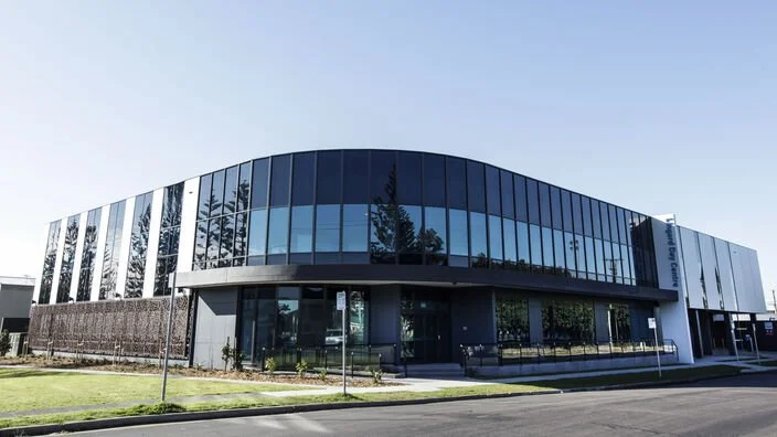 Modern building with glass facade and curved architecture, surrounded by a lawn and street, under a clear blue sky.