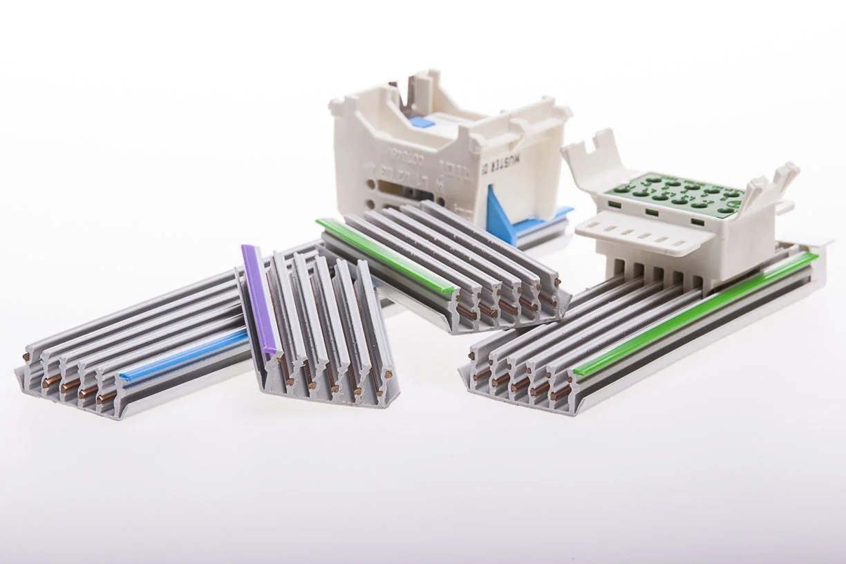 Bauelemente und Komponenten für eine elektrische Schiene, darunter modulare Schienenabschnitte, Klemmelemente und Verbindungsklemmen, auf weißem Hintergrund.