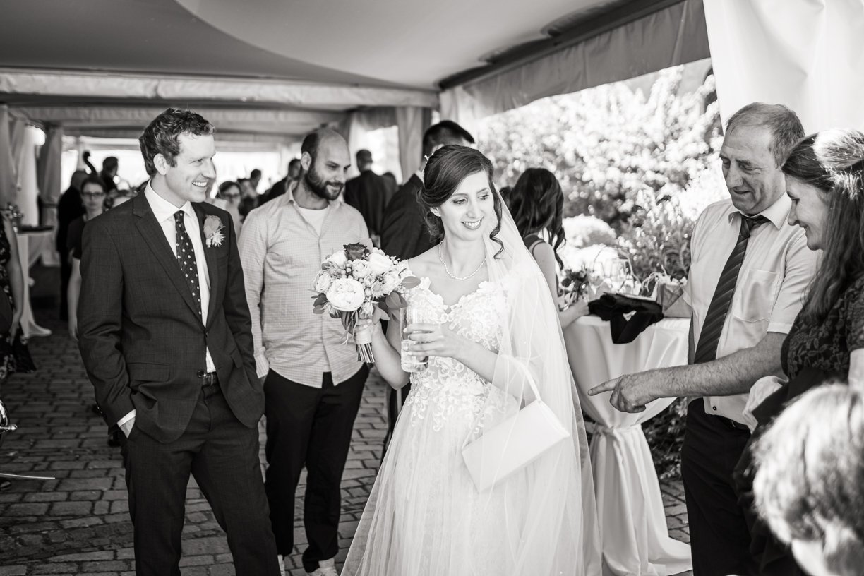 Braut mit Brautstrauß und Freunden bei einer Hochzeitsfeier unter einem Zelt