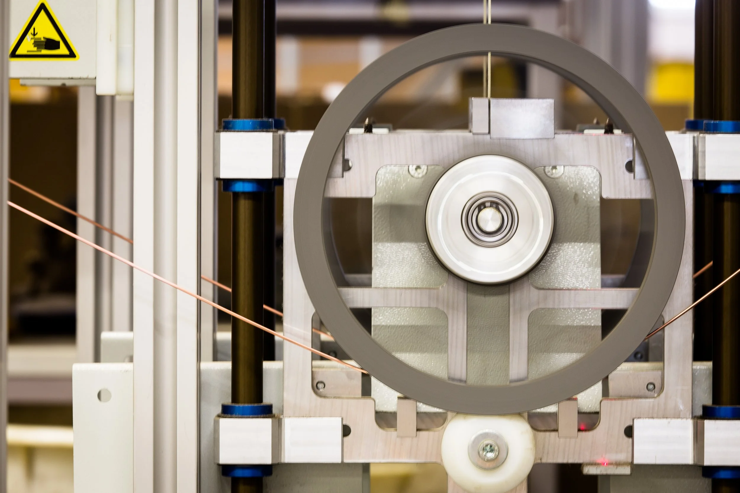 Nahaufnahme eines wissenschaftlichen oder technischen Apparats mit Metallteilen, einer Umlenkrolle und einer Rahmenkonstruktion. Es scheint ein Experiment oder eine Maschine in einem Labor zu sein.