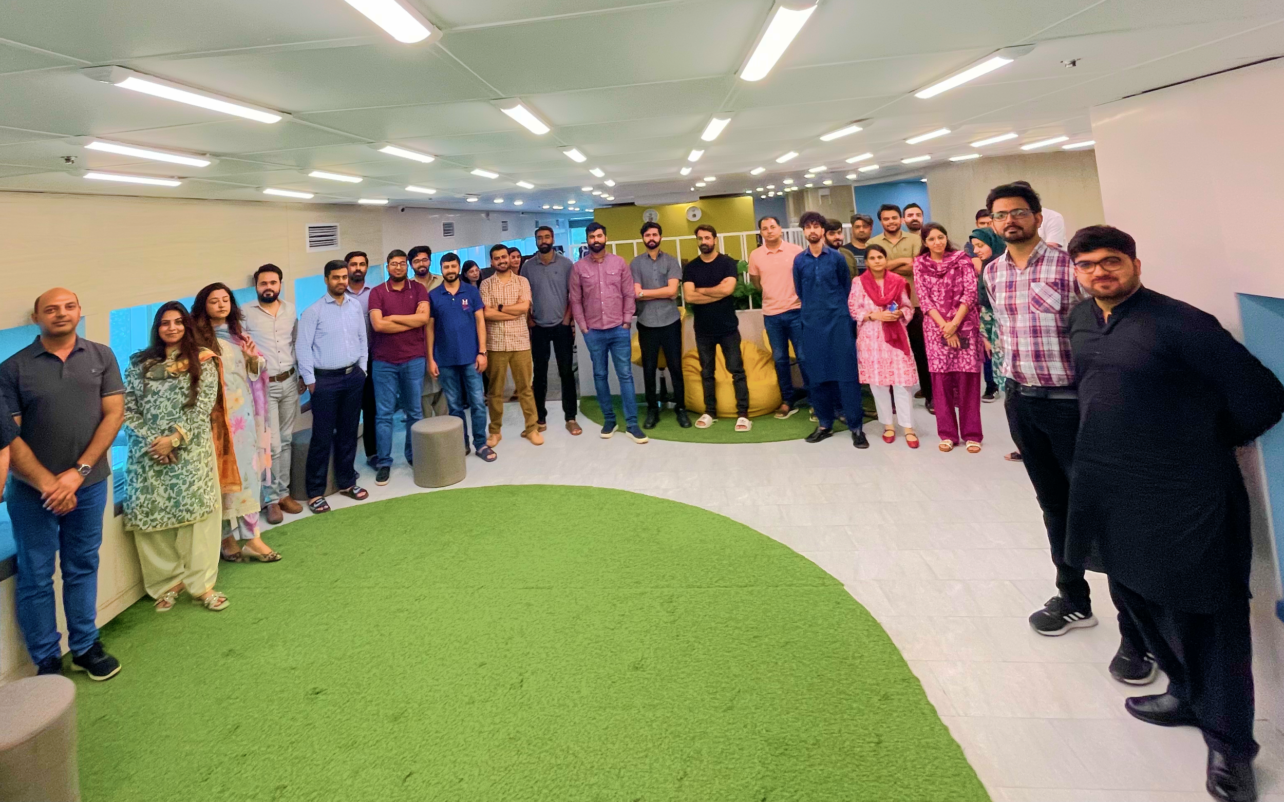 Group of people standing in a semi-circle in an office setting, with a painted green rug in the foreground.