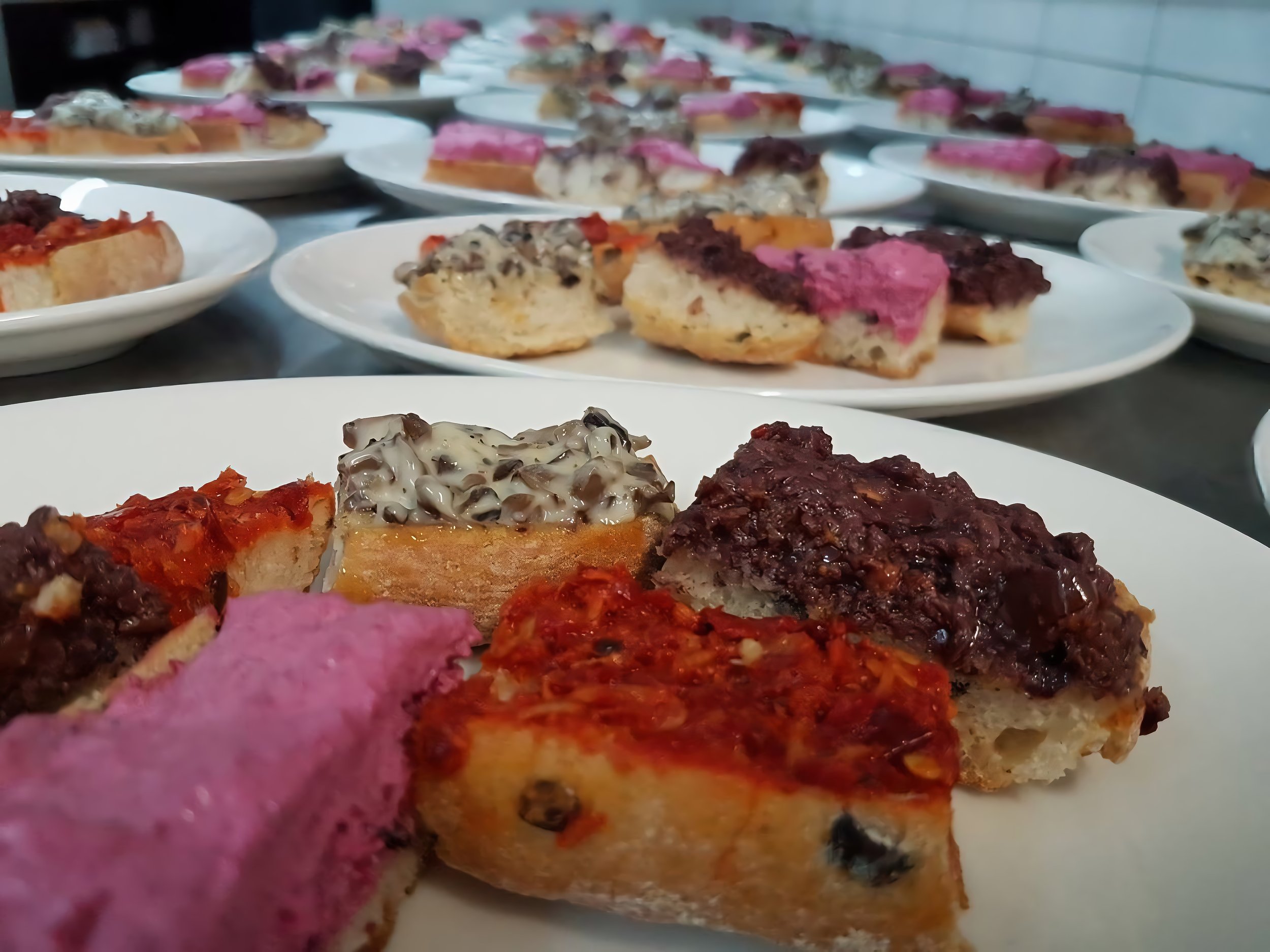 Mehrere weiße Teller mit verschiedenen hausgemachten Bruschette, die auf einer langen Arbeitsplatte der Haus am See Profi-Küche angeordnet sind