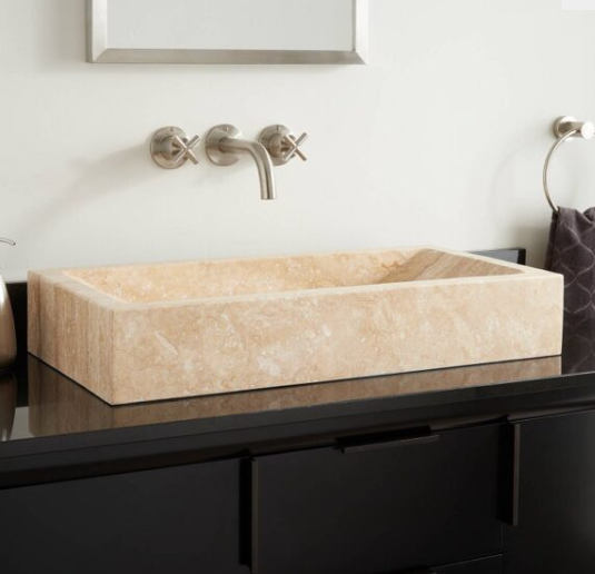 Lavabo en pierre beige posé sur un meuble noir dans une salle de bain moderne.