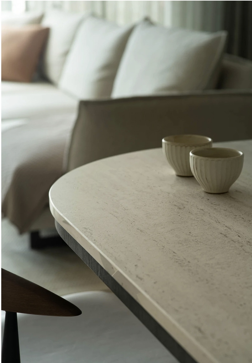 Une table en pierre ou en marbre clair avec deux tasses en céramique, dans un salon moderne avec canapé et coussins en arrière-plan.