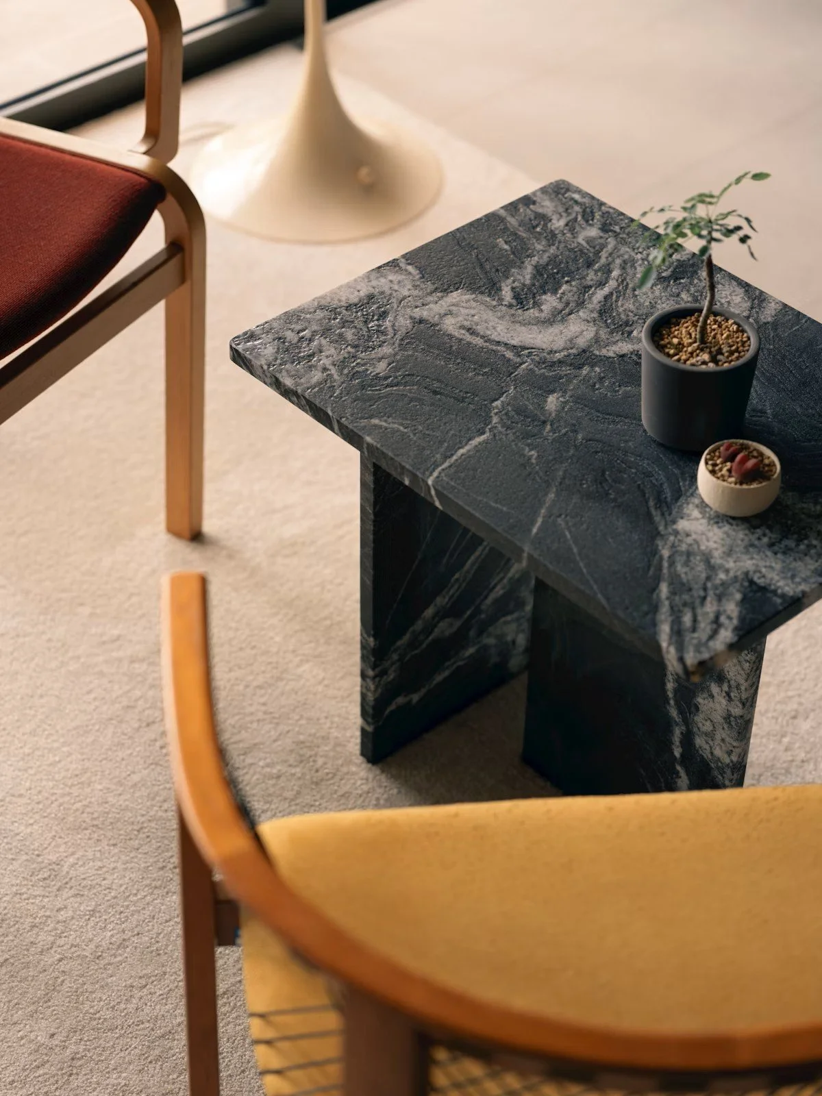 Une table en marbre noir avec veines blanches, décorée d'une plante en pot et de deux petits contenants, dans un intérieur avec un tapis beige et des meubles en bois.