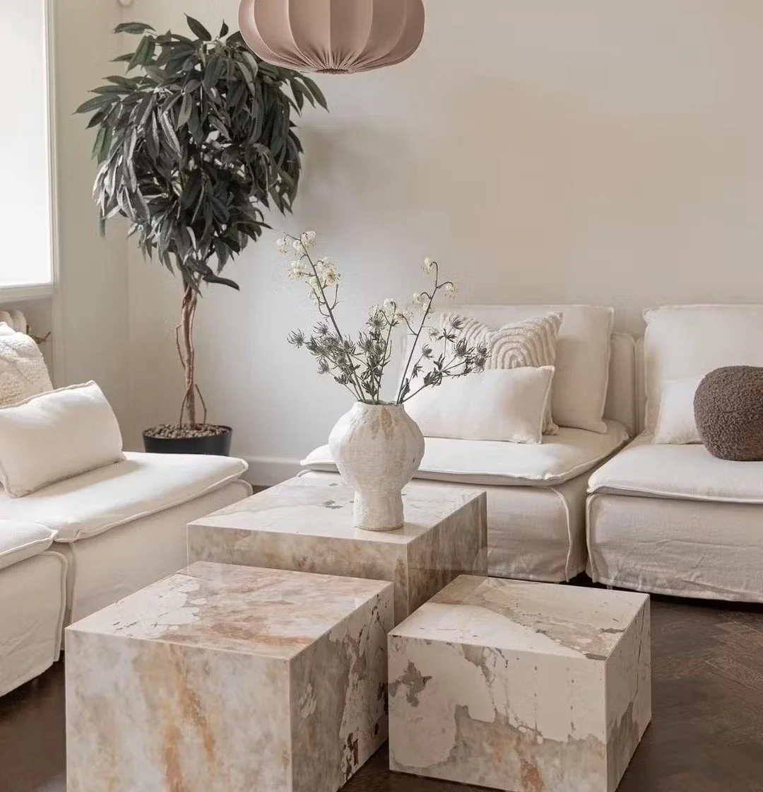 Salon intérieur avec canapé blanc, table en pierre, vase avec des fleurs séchées et une grande plante dans un pot, décoration minimaliste
