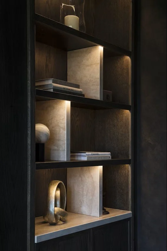 Étagère en bois sombre avec des décorations et des livres, éclairée par des lumières intégrées.